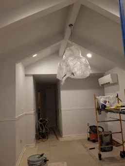 Interior room with sloped ceiling, hanging light fixture, air conditioning unit, and construction tools and equipment.