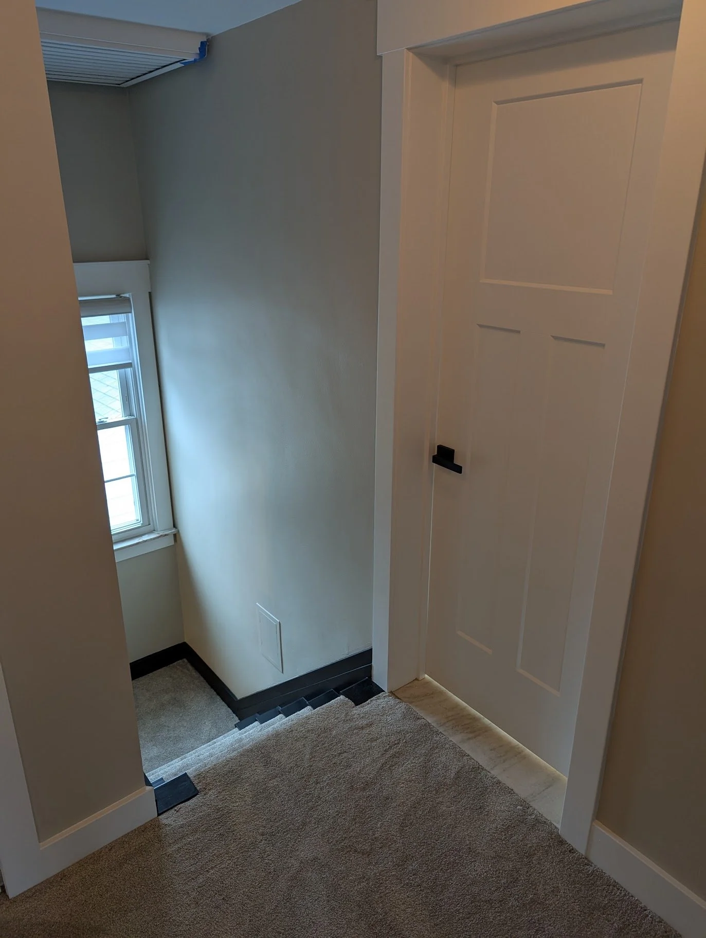 Interior view of a stairway landing area with a window, a closed door to a closet, beige carpeted stairs, and beige walls.