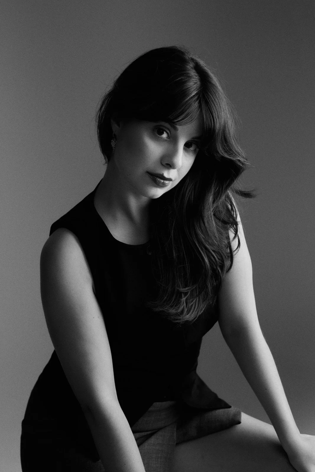 Black and white portrait of a woman with long hair, wearing a sleeveless top, looking at the camera with a slight smile.