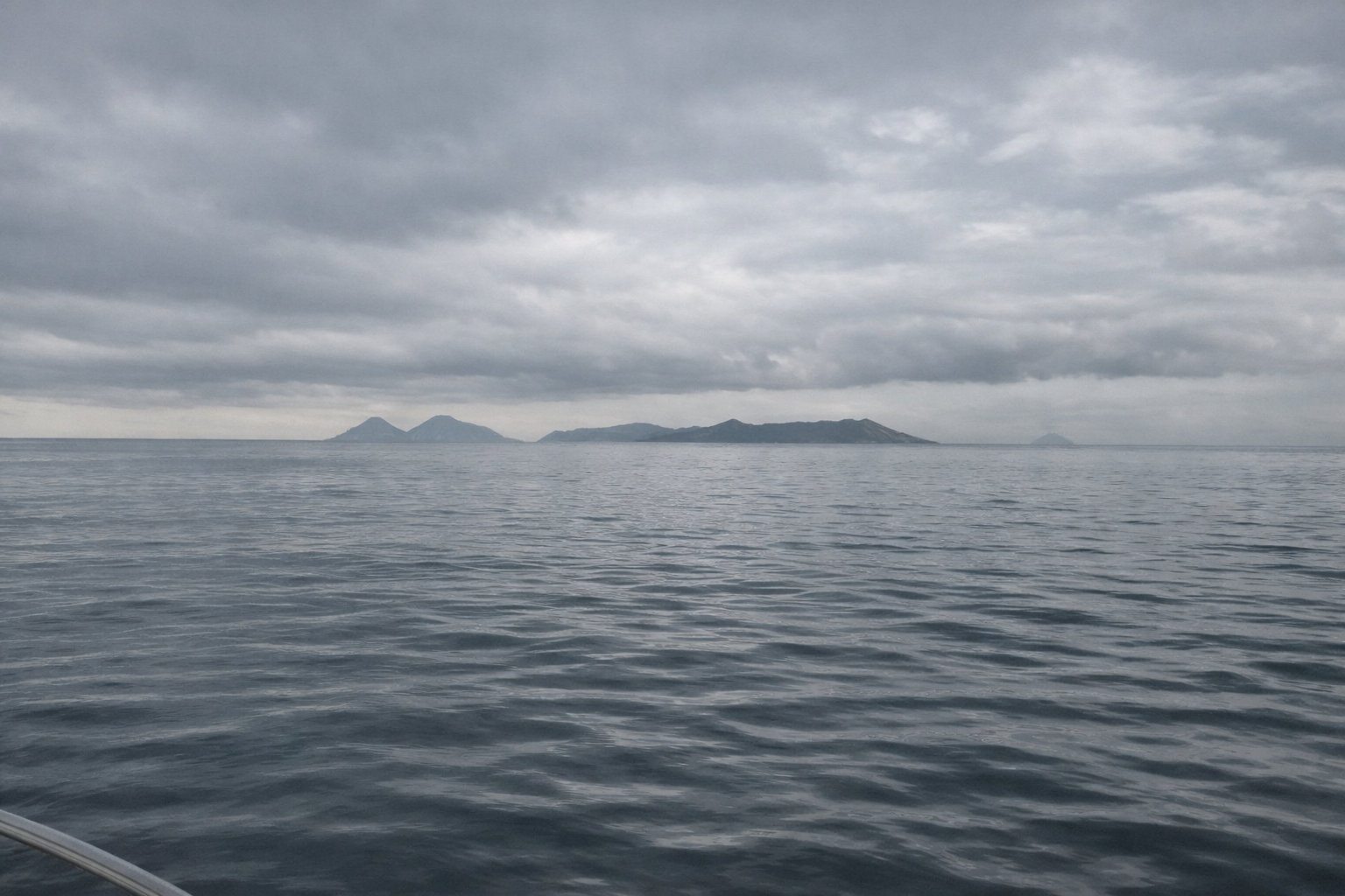 An open ocean horizon with distant mountain islands under a cloudy sky, representing breathwork and altered states of consciousness.