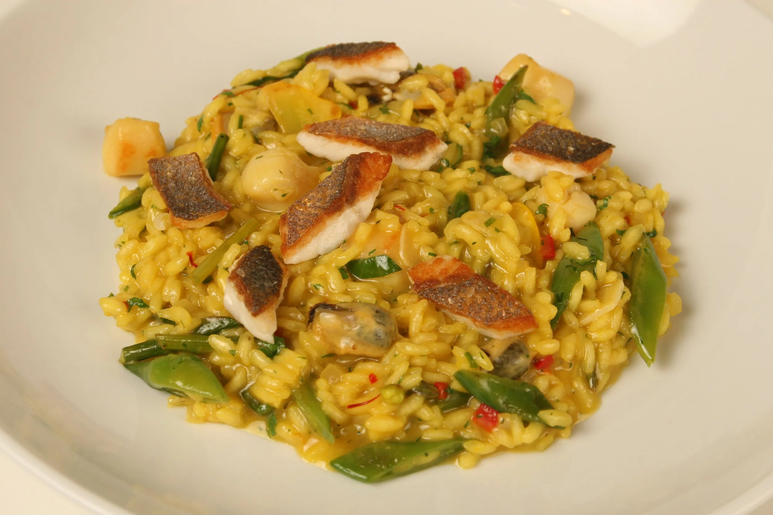 Saffron Risotto al Pescatore with Pan-Seared Branzino, Bay Scallops, PEI Mussels, Littleneck Clams, and Sugar Snap Peas. 