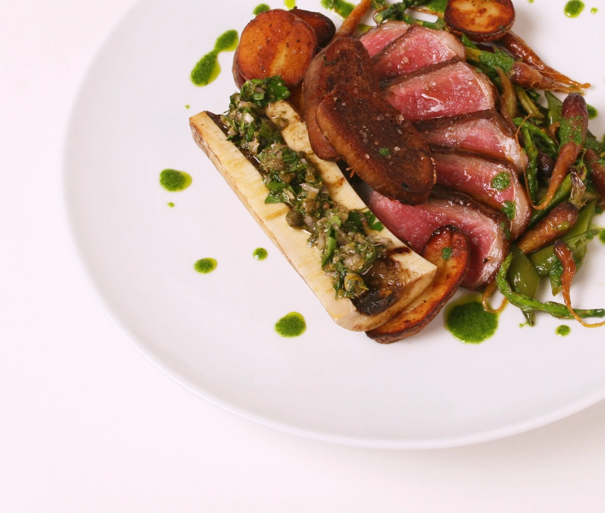 Beef Three Ways: Grilled Ribeye, Crispy Tongue, and Roasted Bone Marrow. Potatoes, Spring Vegetables, and Carrot Top Salsa Verde.