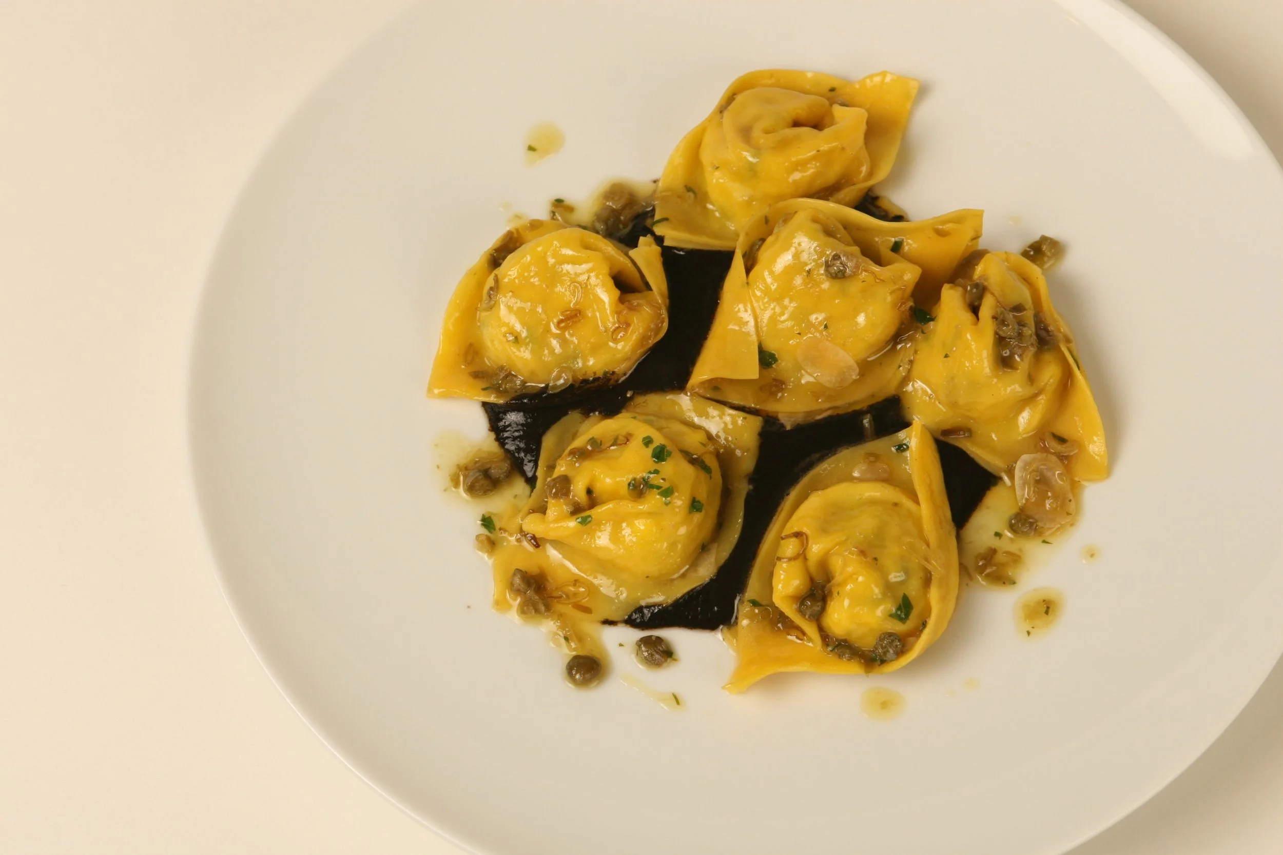 Potato and Salt Cod Tortelli with Green Garlic, Capers, and Squid Ink Ristretto.