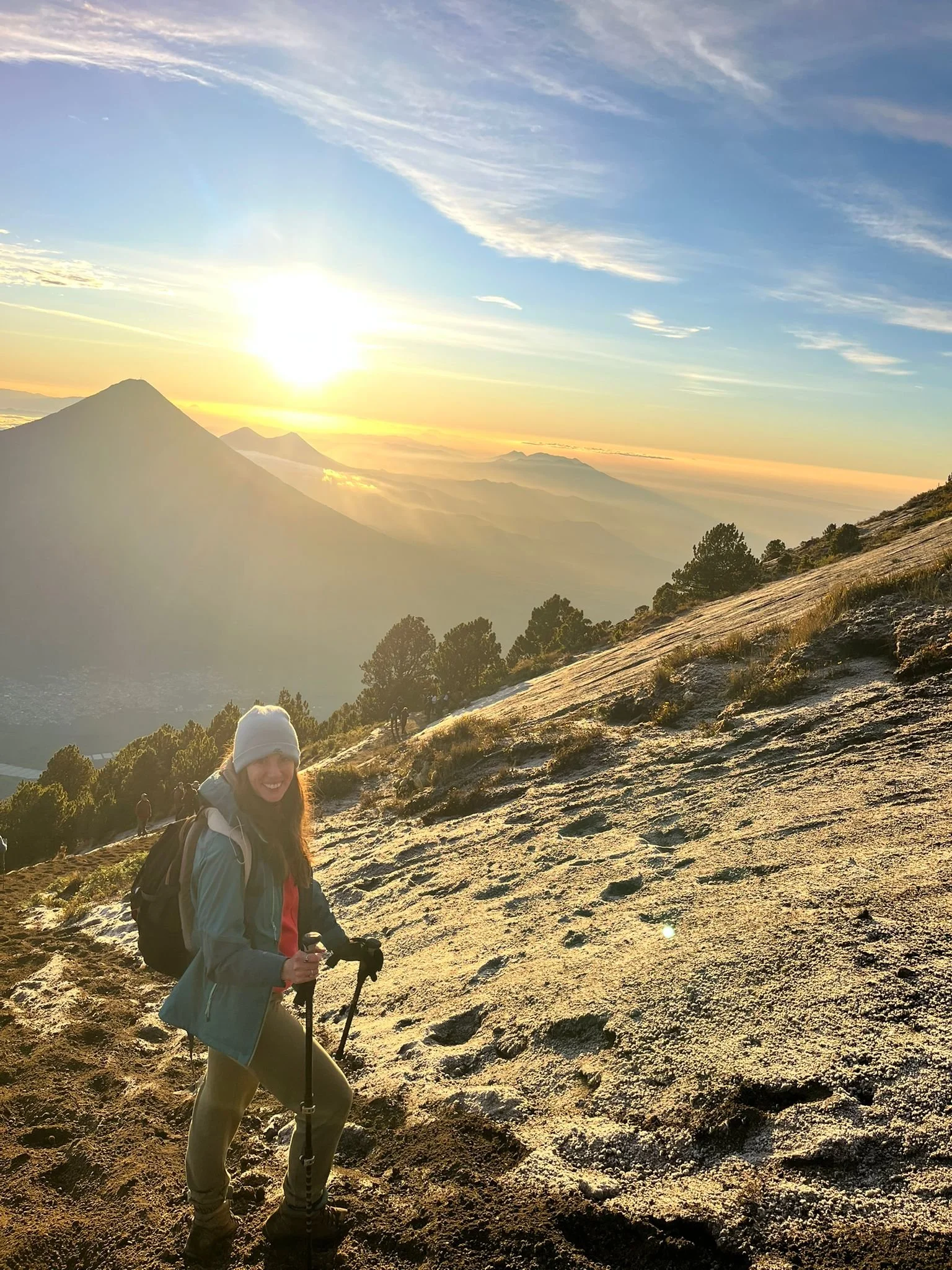 A woman hiking on a trail at sunrise with mountains in the background.