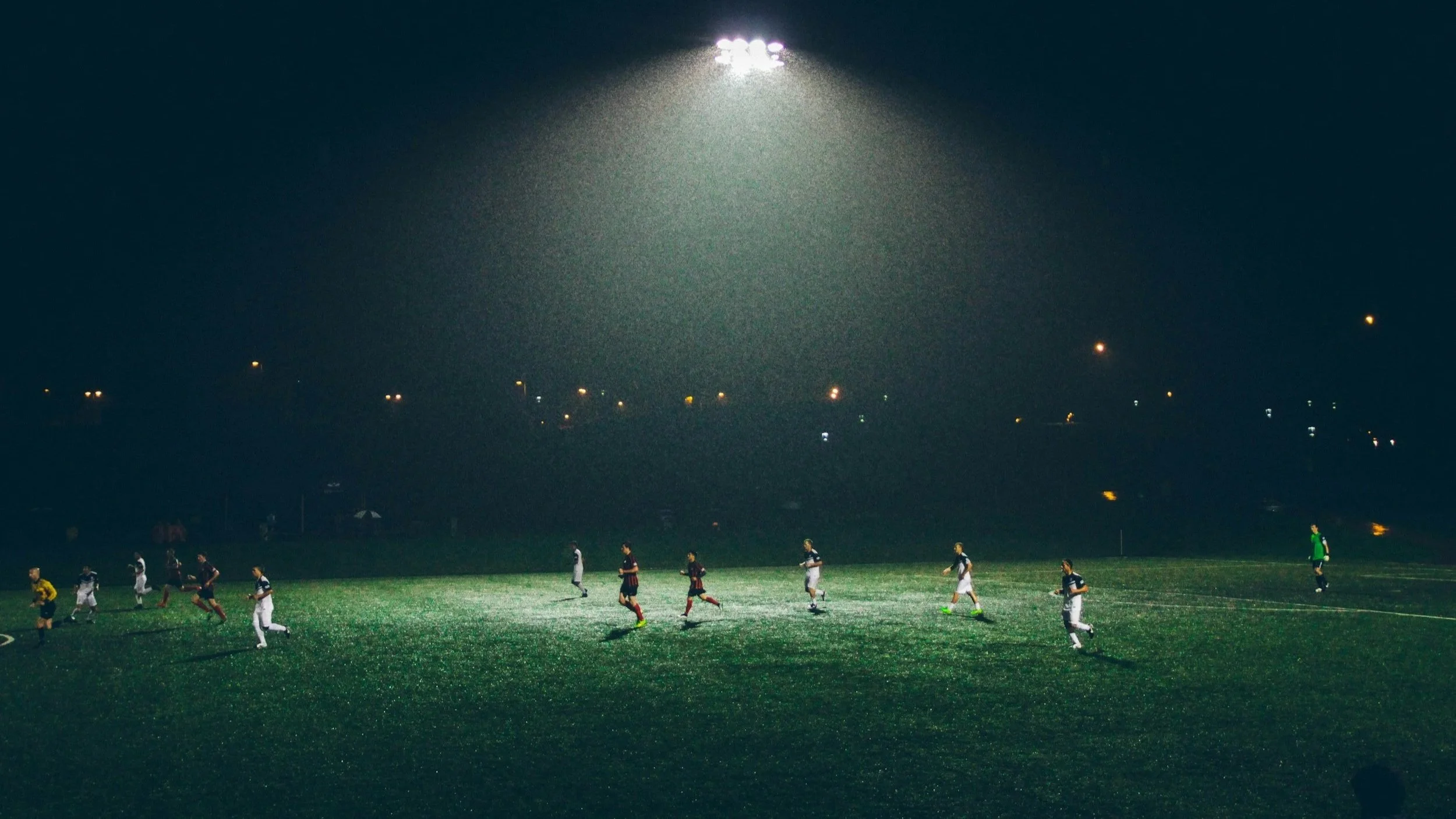 Soccer game taking place at night under floodlights with players on the field.