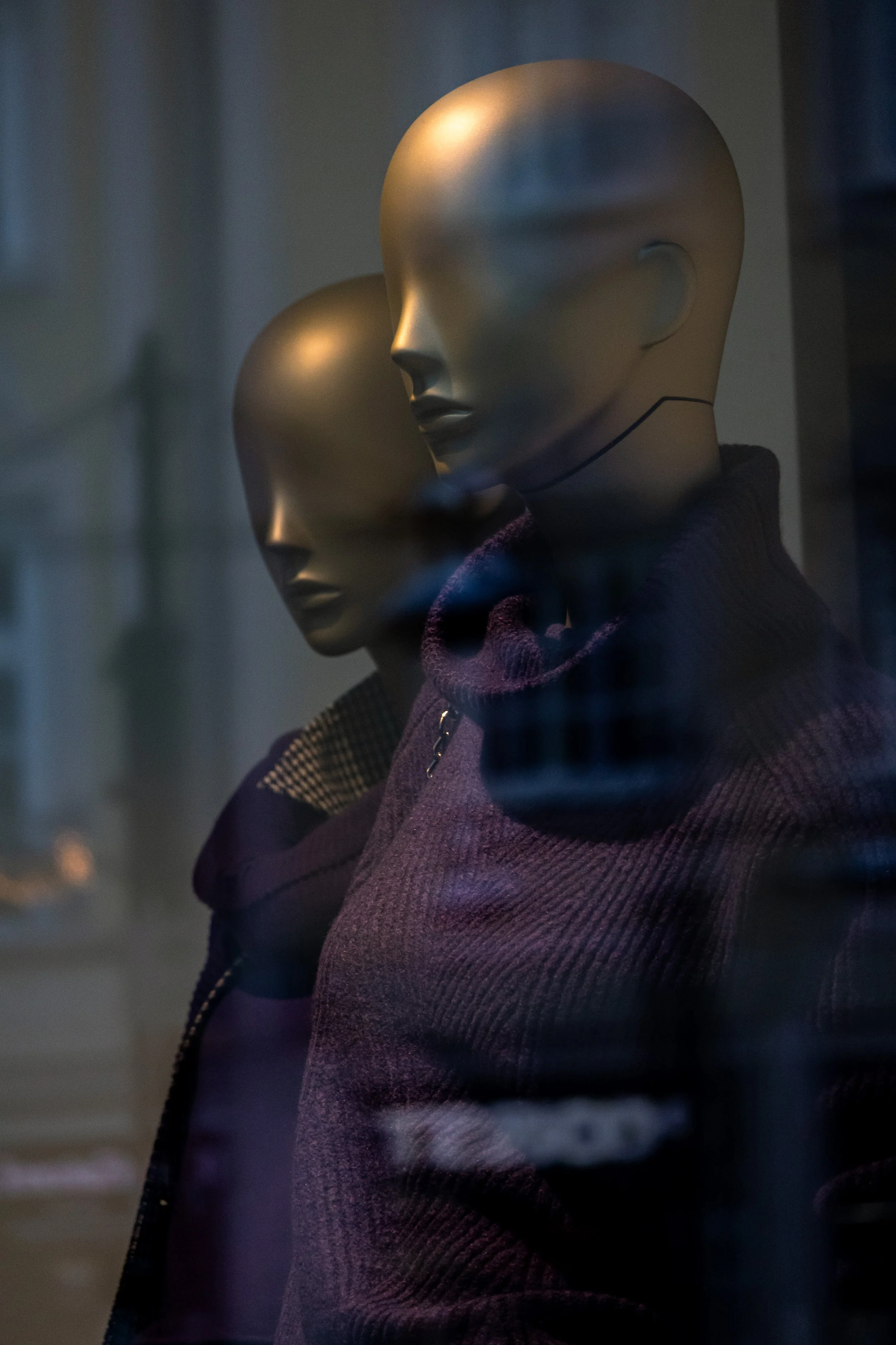 Zwei leere, goldene Mannequins mit dunkler Kleidung im Schaufenster eines Geschäfts bei Nacht.