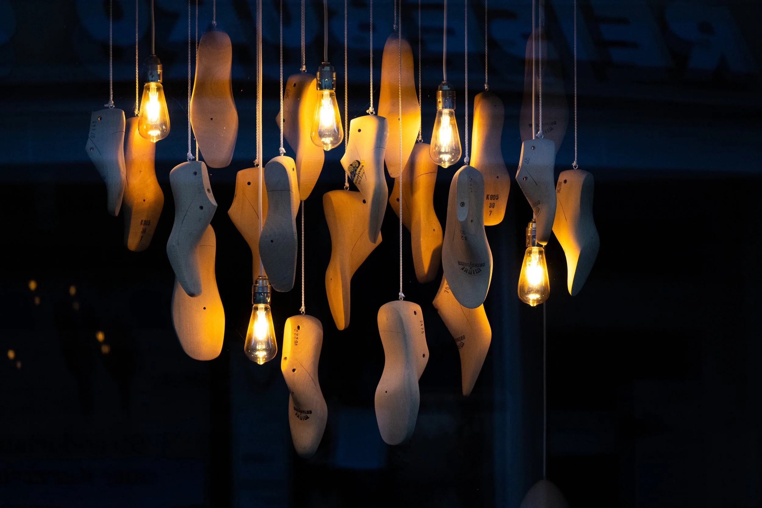 Hängende Lichtquellen, bestehend aus Glühbirnen und Holzformen, in dunklem Raum.