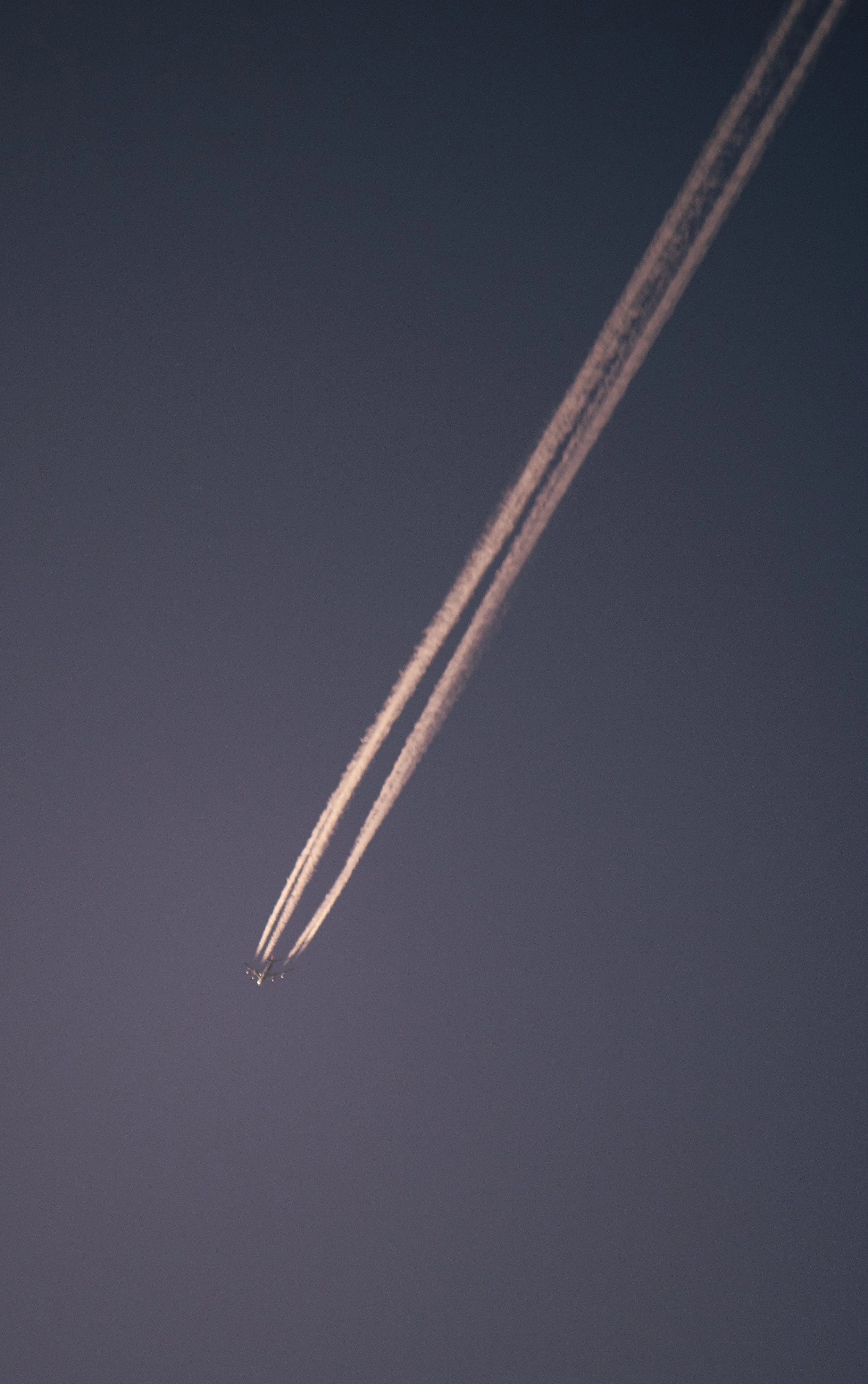 Der Himmel ist dunkel mit zwei Flugzeugen, die Kondensstreifen hinterlassen, die sich diagonal kreuzen.