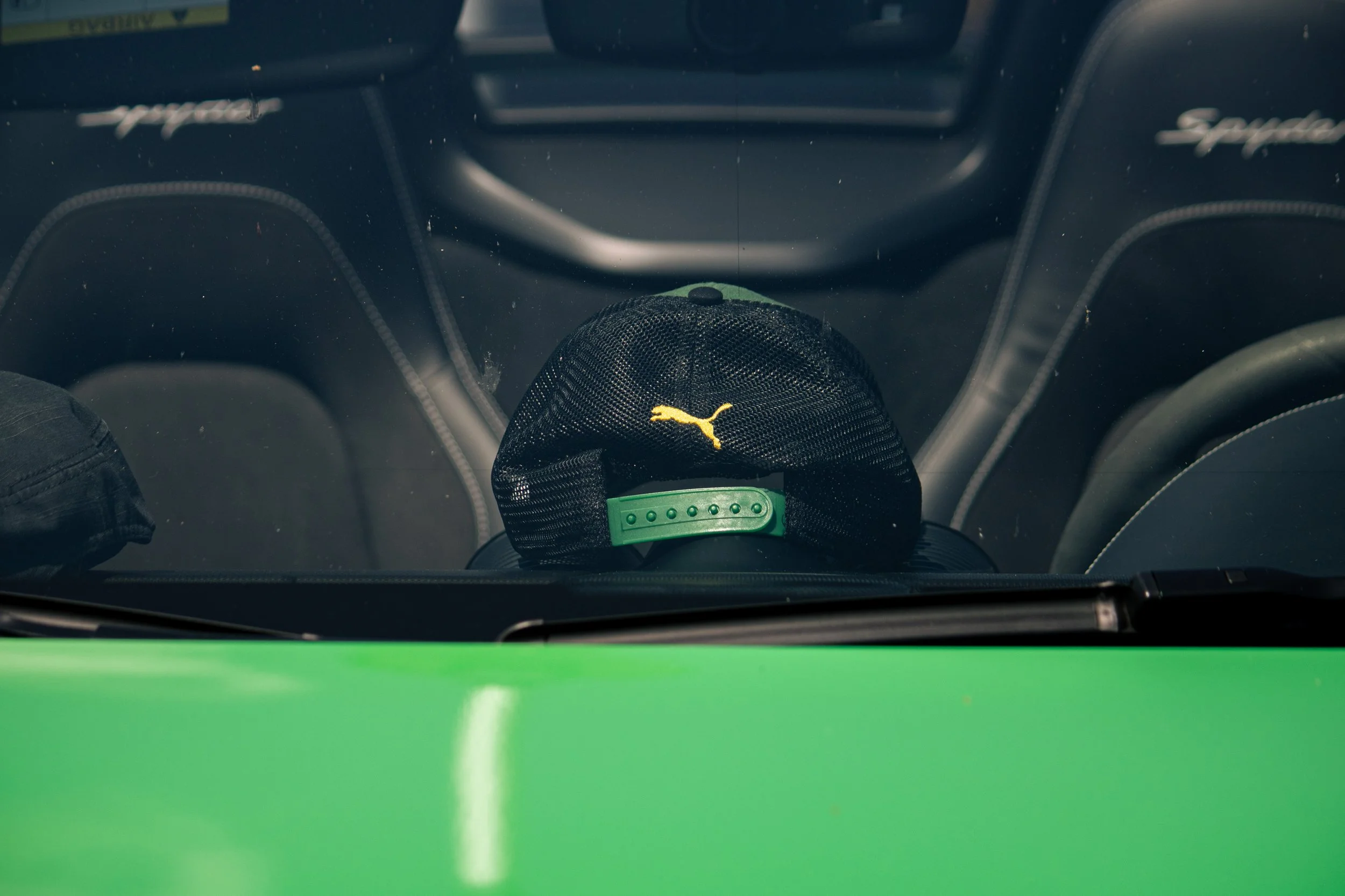 Blick von oben auf das Innere eines Autos, auf der vorderen Sitzbank liegt eine schwarze Mütze mit einem gelben Puma-Logo, im Hintergrund sind die Armaturen und das Lenkrad sichtbar.