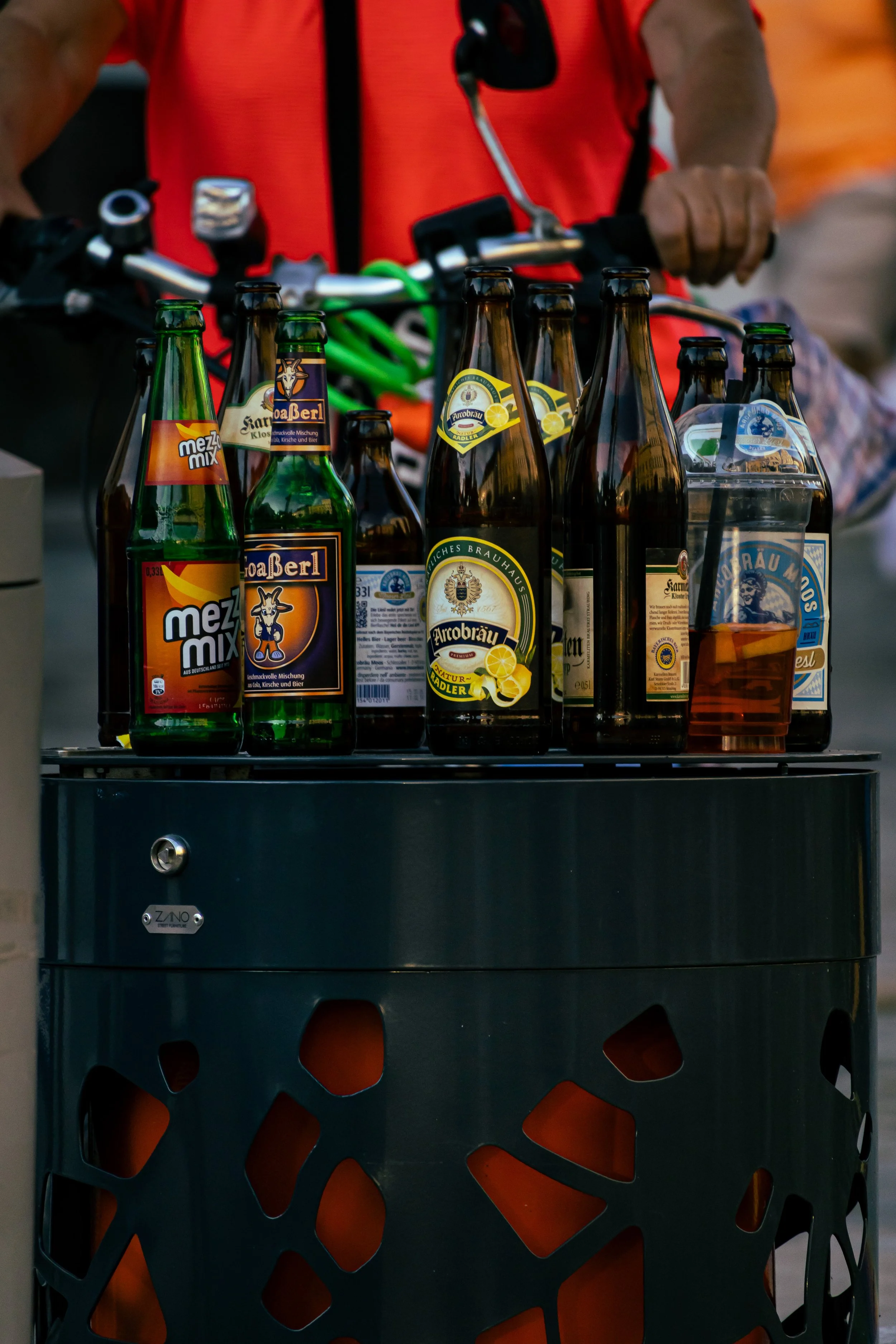 Ein Mann in rotem Topf, der eine Vielzahl von Bierflaschen auf einem Lautsprecher platziert.