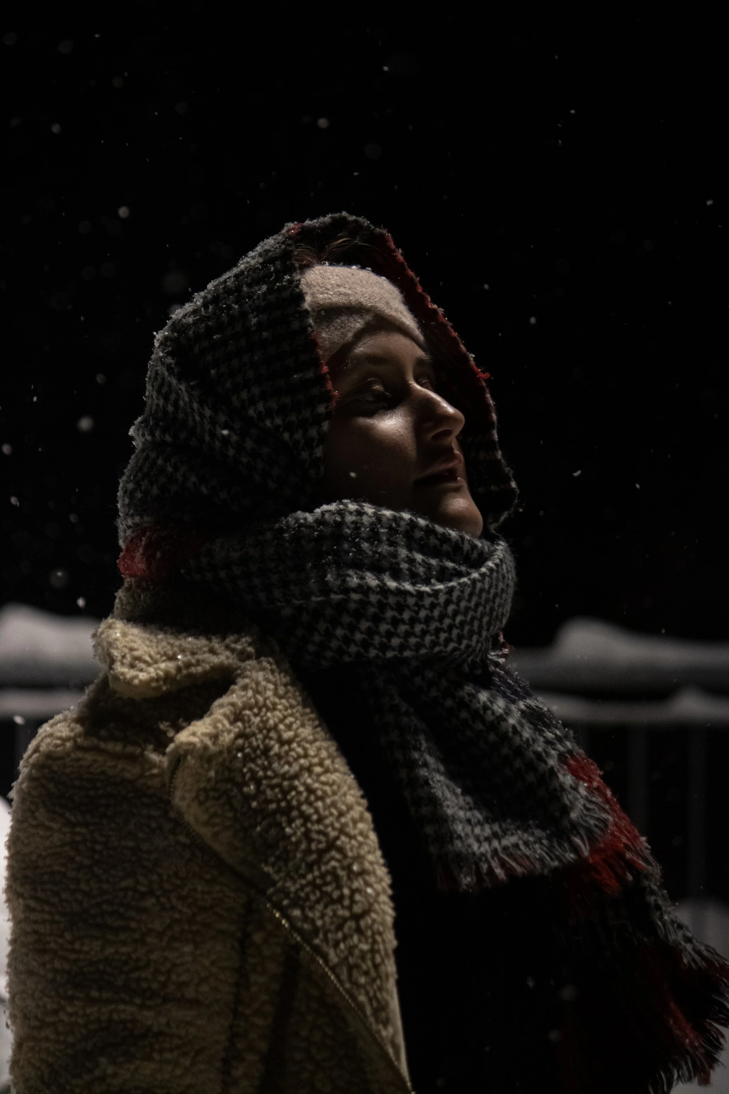 Nahaufnahme eines jungen Mannes mit Mütze und Schal bei Schneefall in der Nacht.