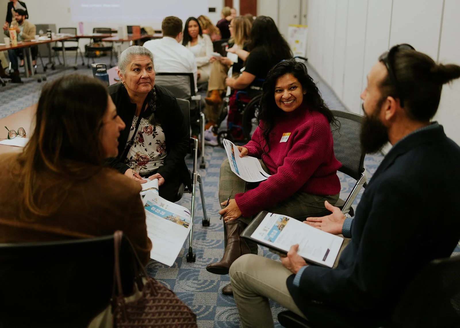 Group of diverse people sitting in a circle, engaging in conversation at a professional event or workshop in a conference room.