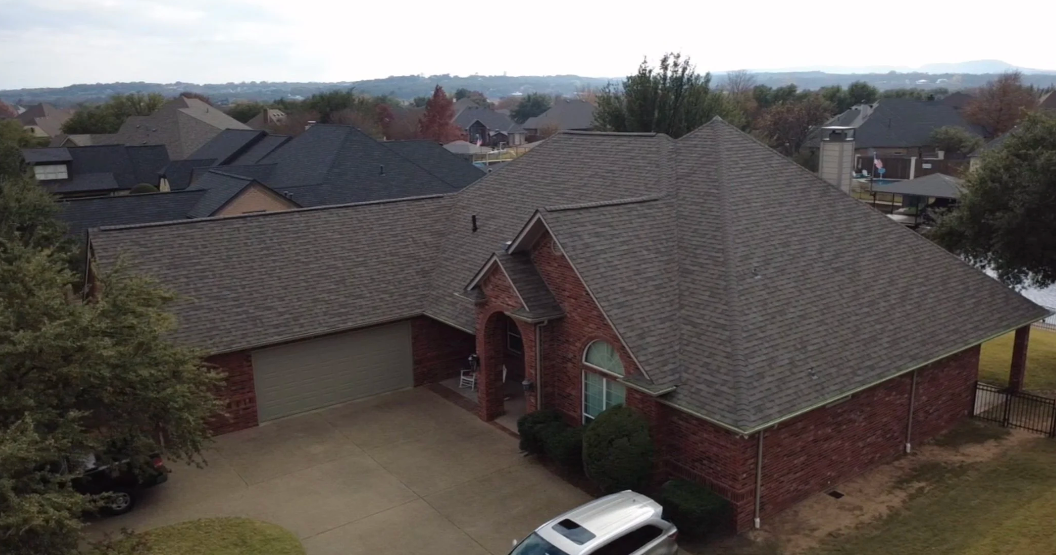 Aerial view of rooftops in a suburban neighborhood with trees and distant hills.