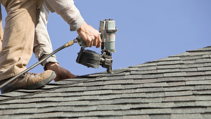 Worker installing or repairing shingles on a roof using a pneumatic nail gun.