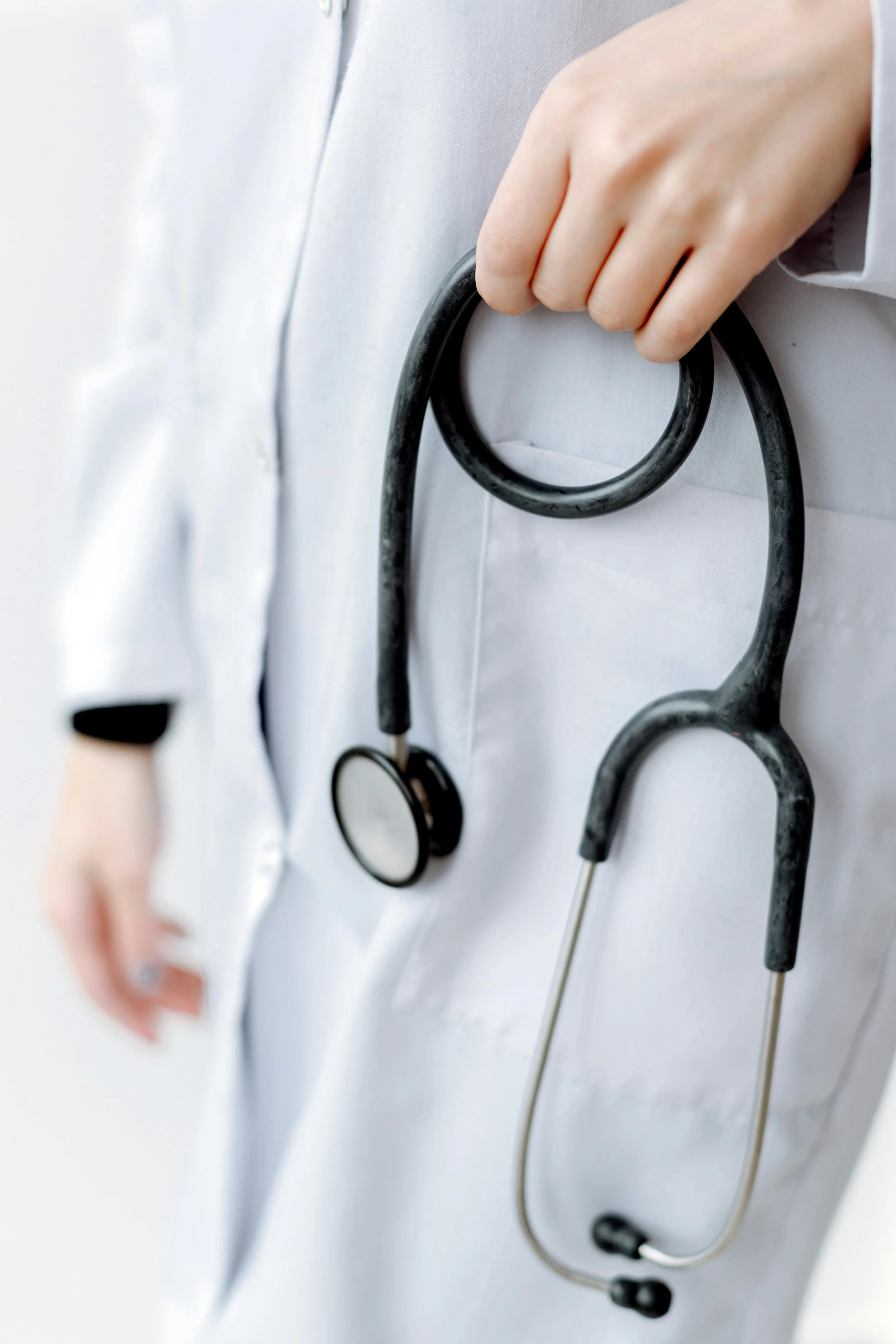 A person's hand holding a stethoscope against a white medical coat.