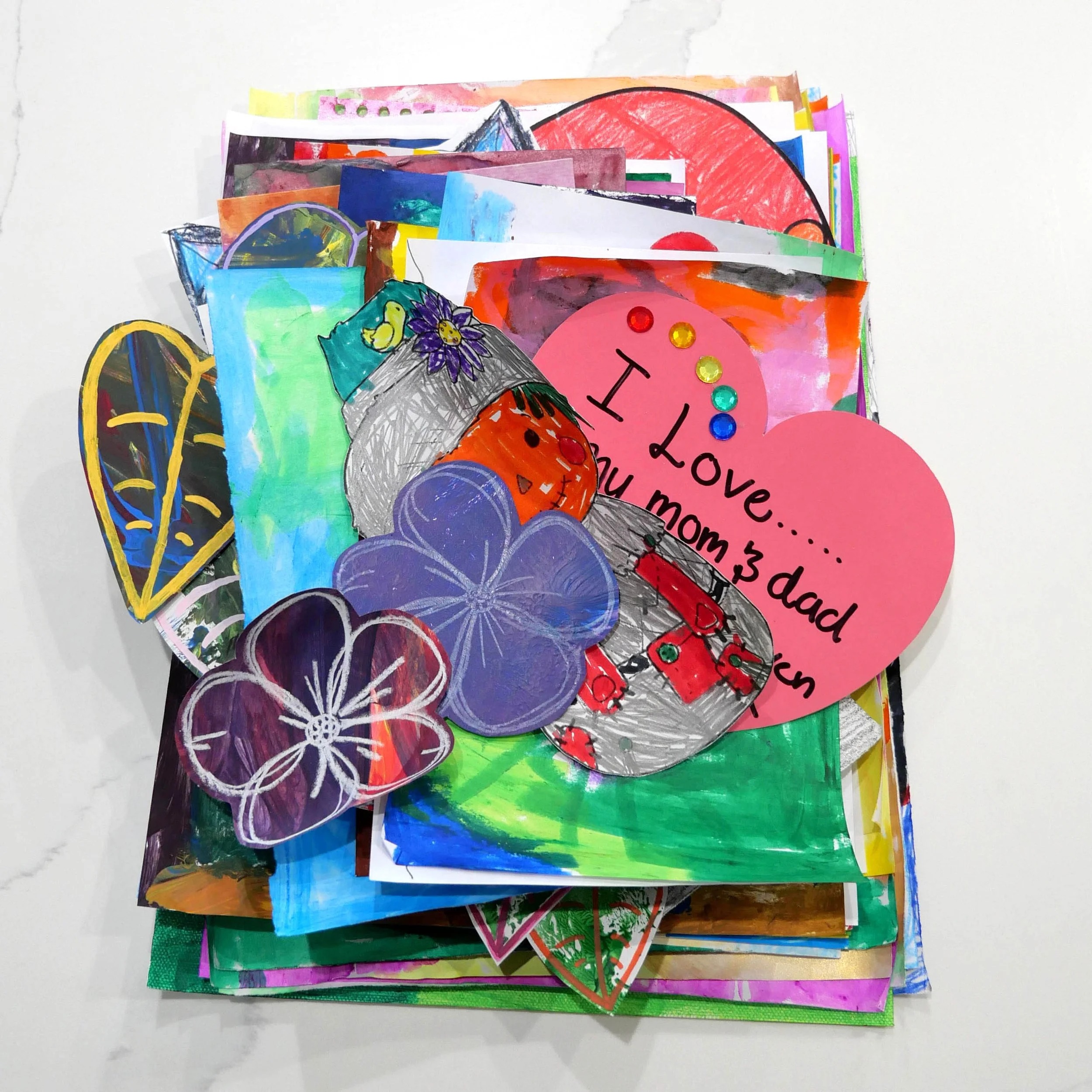 A stack of colorful drawings and cards, some with floral and heart designs, on a white surface.