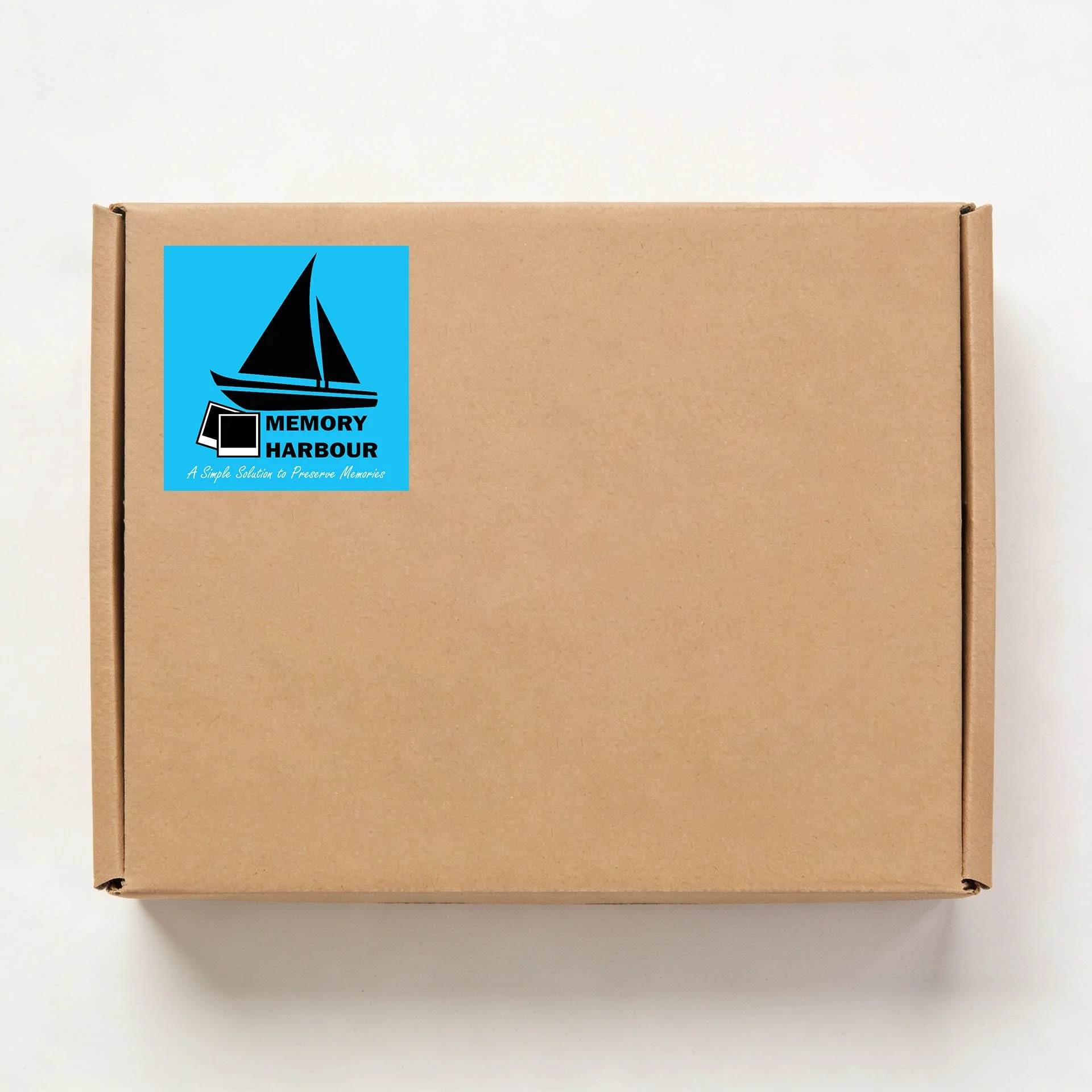 A plain cardboard box with a blue logo and text that reads "Memory Harbour" on the front. The logo features a stylized black sailboat next to a small black rectangle. The lower part of the logo includes a slogan in cursive that says "A Simple Solution to Preserve Memories." The box is placed on a white surface with a neutral background.
