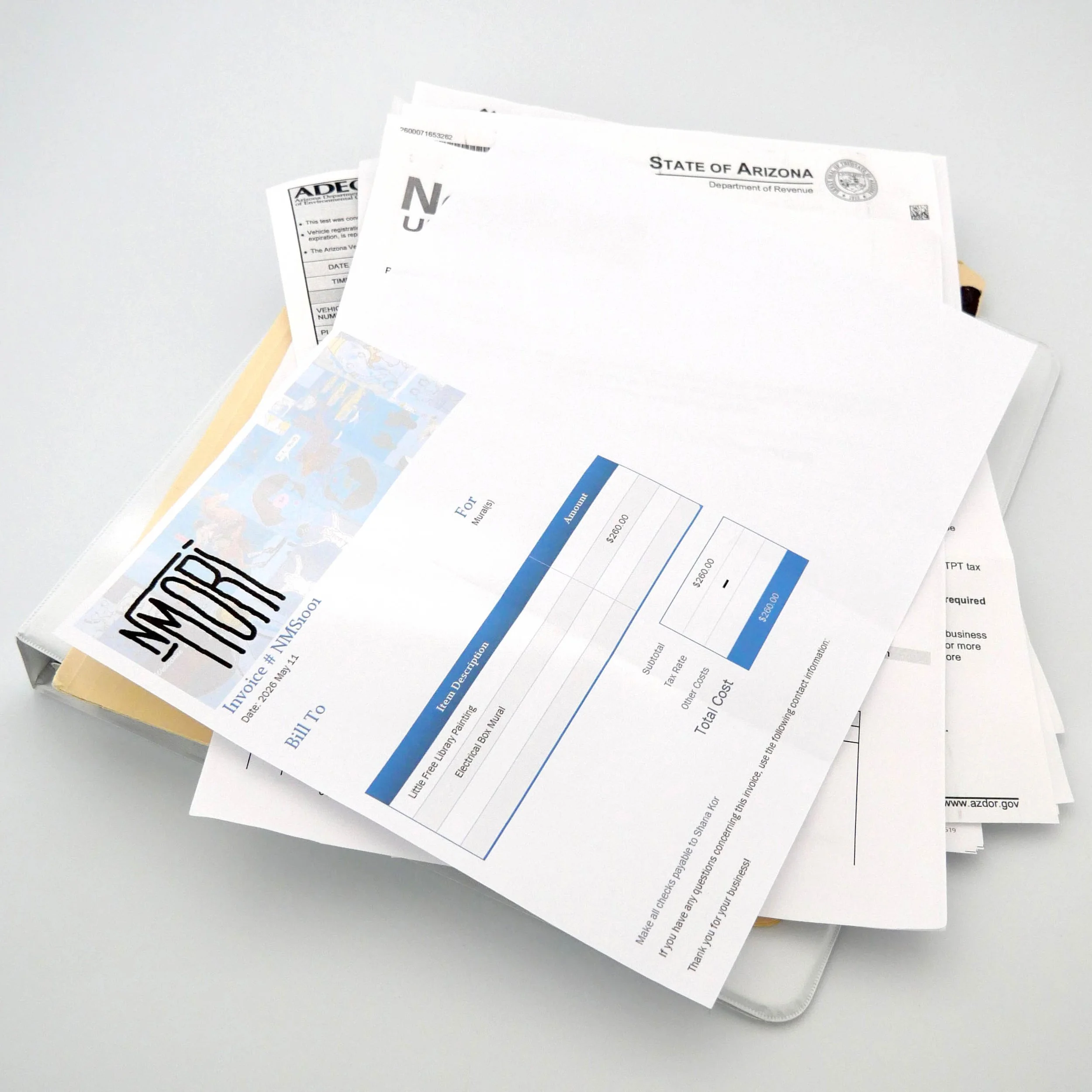 A stack of important documents, papers, and bills, including a notice from the Arizona Department of Revenue, on a white surface.