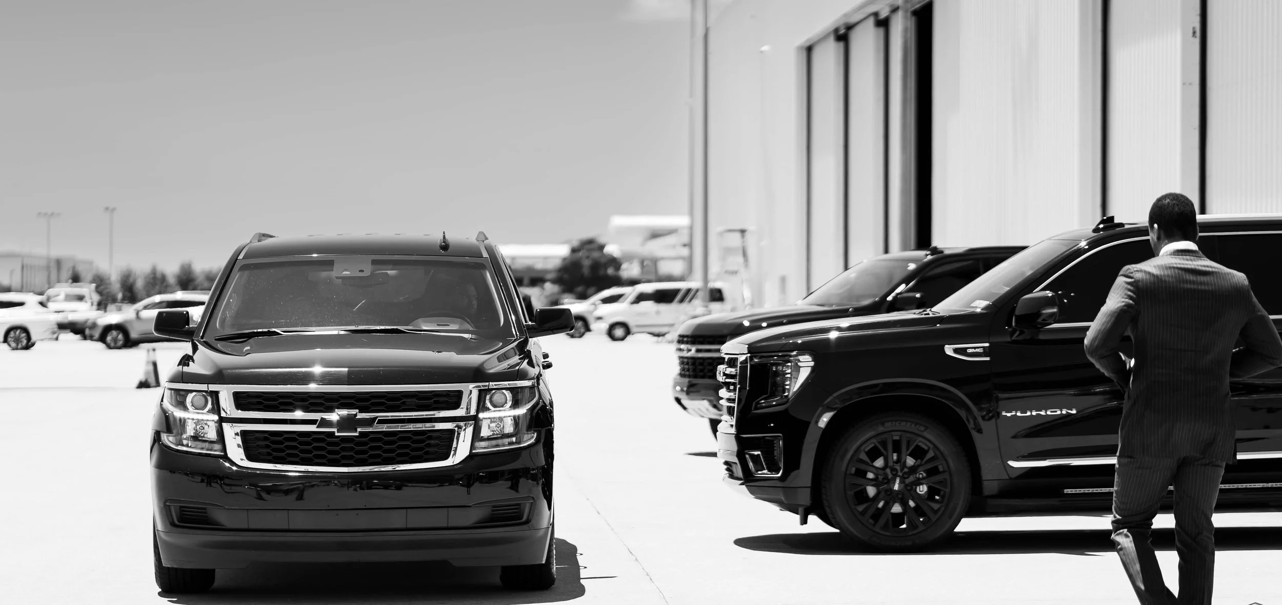 Black SUVs parked in a lot with a man in a suit walking nearby.