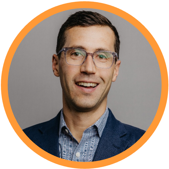 Kevin Horn, CEO. A young man with short dark hair, glasses, and a light complexion, smiling and wearing a dark blazer over a light button-up shirt. The background is plain gray with an orange circular border.