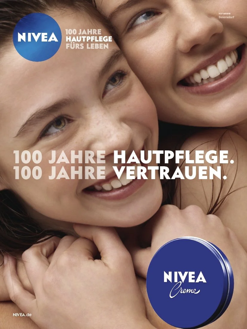 Photo de deux jeunes filles souriantes, avec un fond blanc, célébrant le 100e anniversaire de Nivea, en allemand, avec un emballage de crème Nivea en bas à droite.