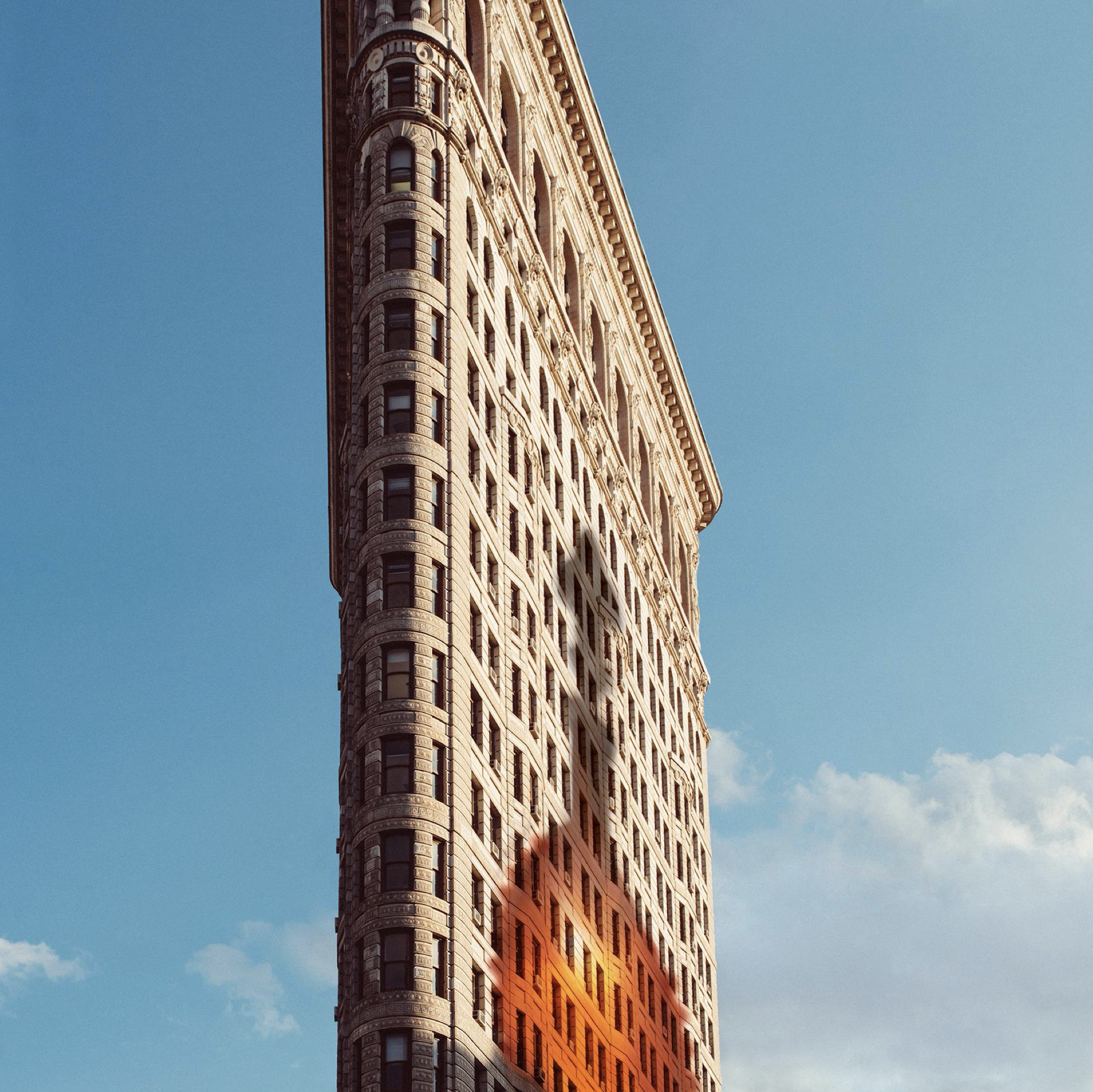 Un immeuble en pierre de style ancien avec de nombreuses fenêtres, photographié en angle contre un ciel bleu clair.