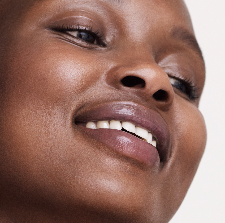 Un gros plan du visage d'une femme noire souriante avec peau lisse et lèvres pulpeuses.