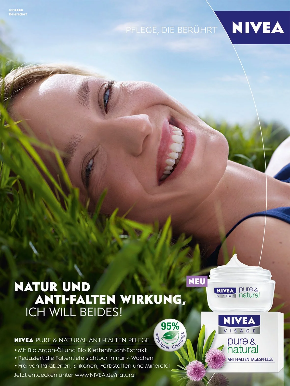 Une femme souriante allongée dans l'herbe avec un ciel bleu, publicité pour le soin anti-rides Nivea à base d'ingrédients naturels, mettant en avant la réduction des rides et l'utilisation d'huile d'argan bio et d'extrait de figue de barbarie.