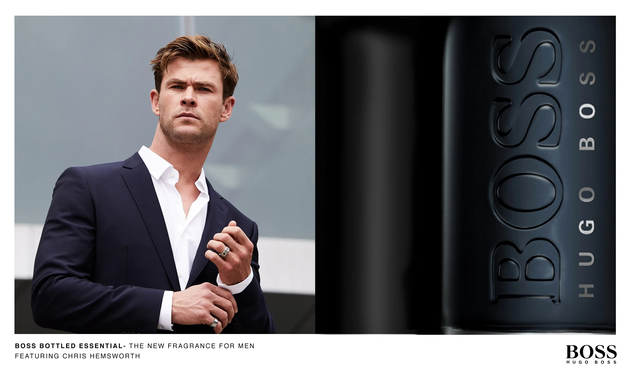 Un homme en costume noir portant une montre et un anneau, posant devant un bâtiment moderne, à côté d'une publicité pour une nouvelle fragrance homme de Hugo Boss.