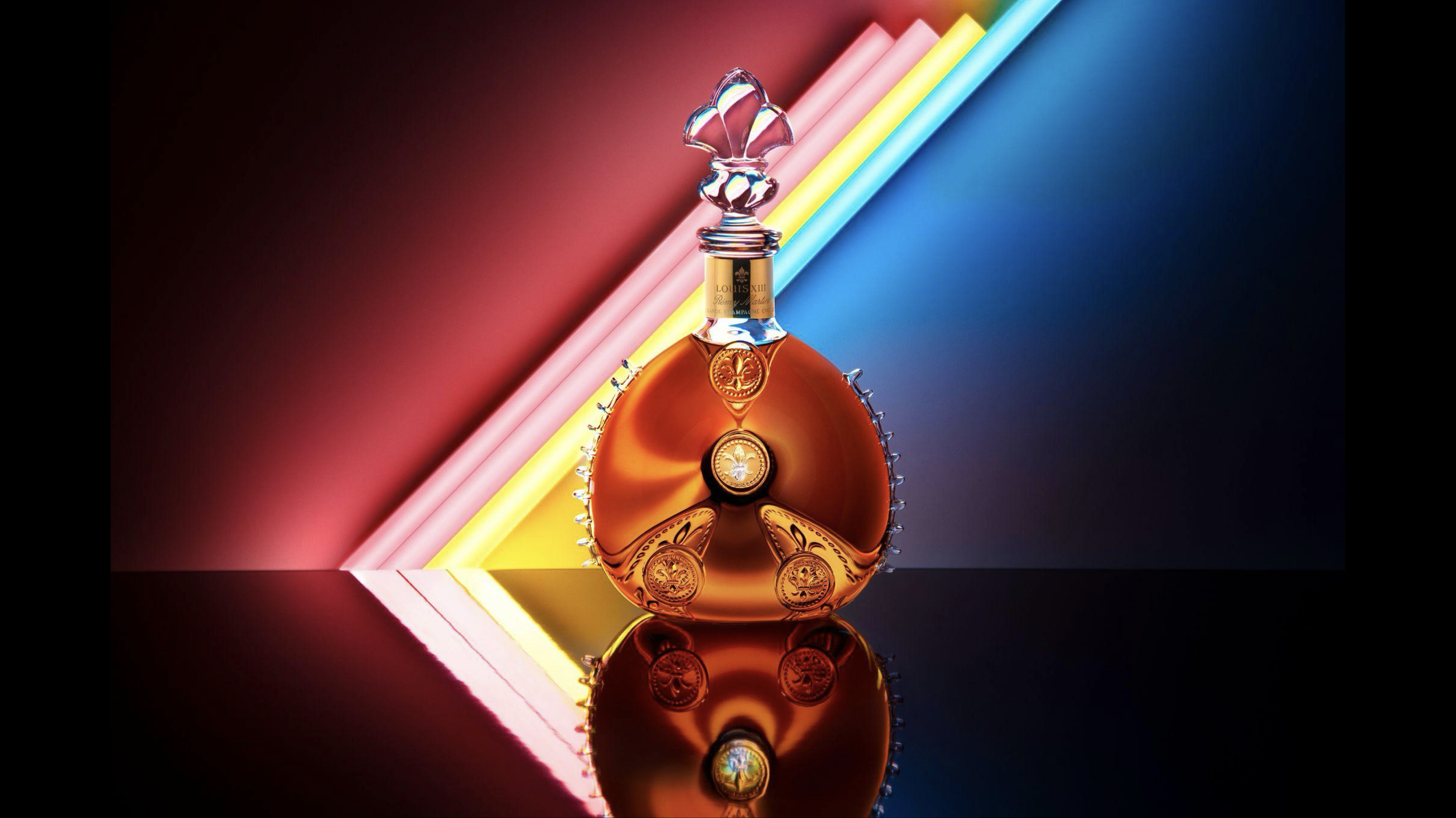 Une bouteille de parfum ornementée posée devant un fond noir avec des lignes de lumière colorées en rose, jaune et bleu, créant un effet de reflet en dessous.
