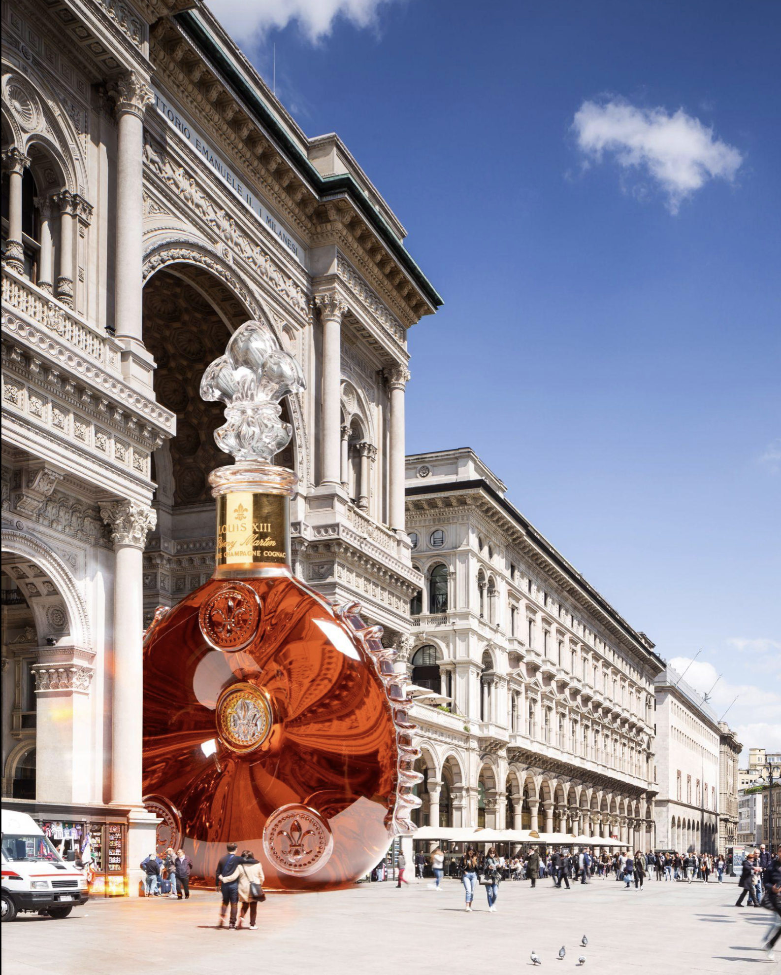 Une grande place animée avec une sculpture en verre orange représentant un dauphin, entourée de bâtiments historiques en architecture néoclassique sous un ciel bleu avec quelques nuages.