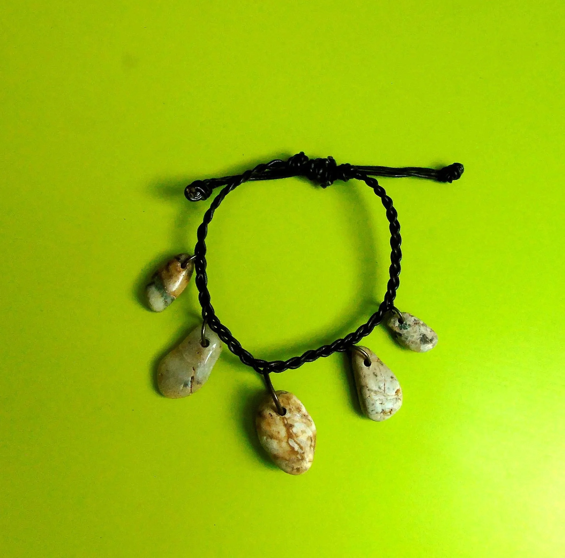 Close-up of a black chain necklace with irregularly shaped white stones on a bright green background.