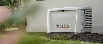 A Generac generator outdoors near a building with grass and trees in the background.