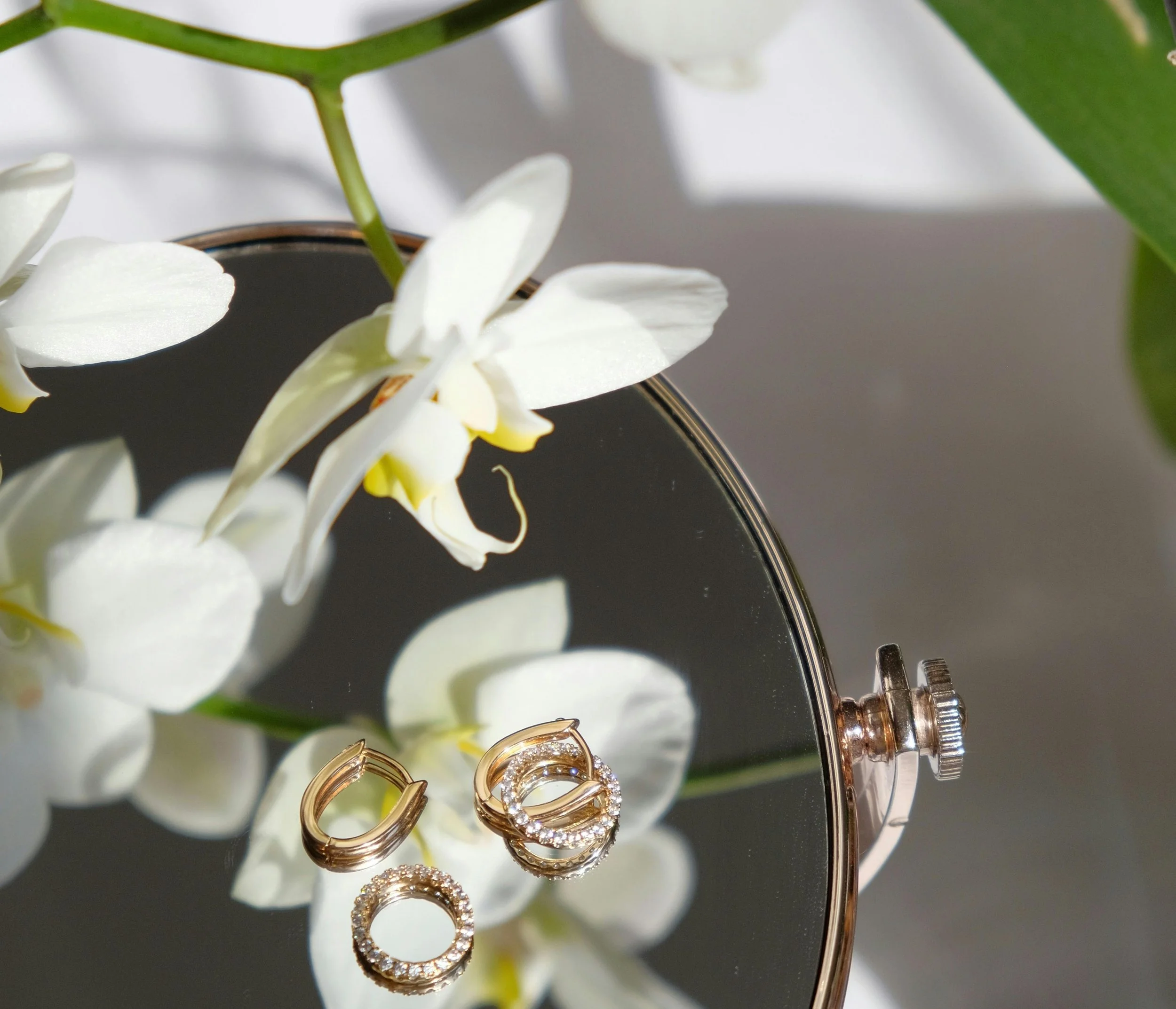Close-up of gold and diamond hoop earrings hanging on a jewelry display with white orchids in the background.