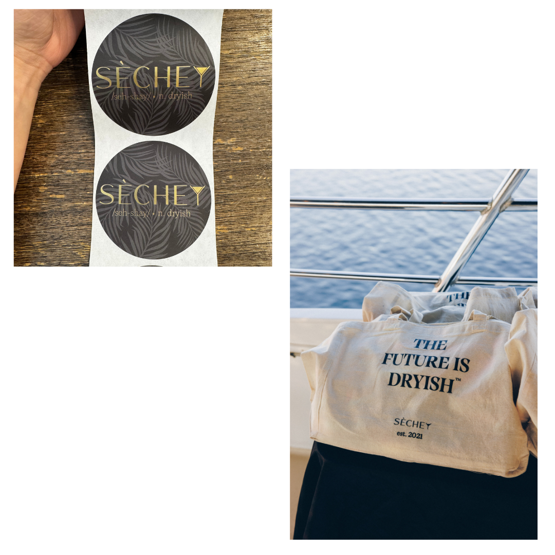 A hand holding a vertical strip of two round stickers with the brand name 'SEÇHEY' and the tagline 'seh shay' n. dryish' on a wooden surface, and a canvas tote bag with the text 'THE FUTURE IS DRYISH' and 'SEÇHEY est. 2021' printed on it, placed on a table near a boat with a view of the ocean in the background.