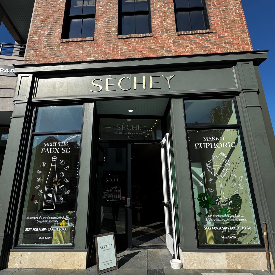 storefront of SECHEY, a shop selling alcohol-free cannabis and wine. The windows feature promotional posters with slogans 'Meet the Faux-Sé' and 'Make it Euphoric,' including illustrations of a bottle and a cocktail glass, respectively. The entrance is open, revealing an interior with a counter and display area.