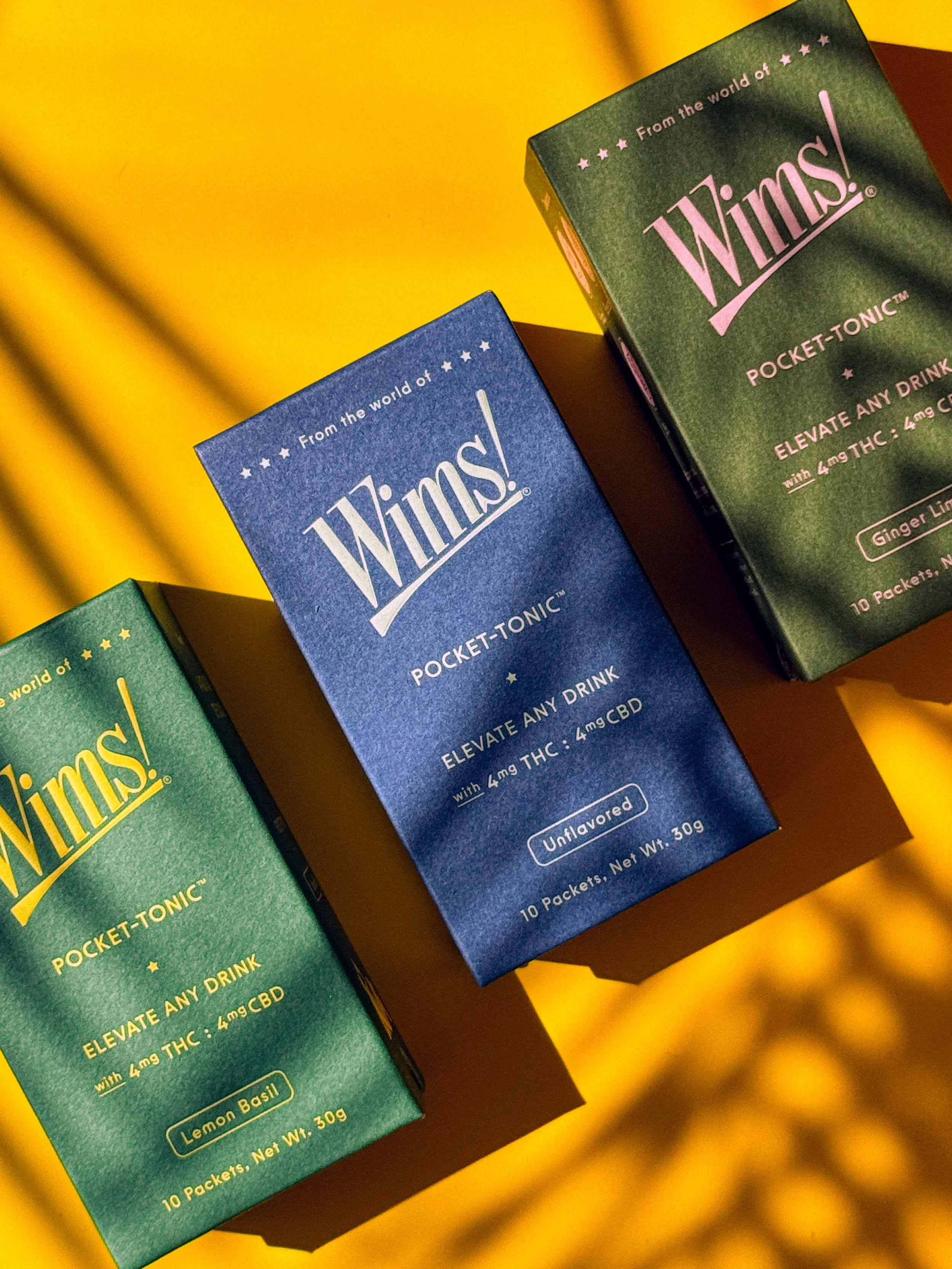 Close-up of three boxes of Windsor Pocket-Tonic, a CBD beverage, on a yellow surface. The boxes are green, blue, and dark green, with text indicating they contain 10 packets of unflavored CBD drink mix, each with 4 mg THC.