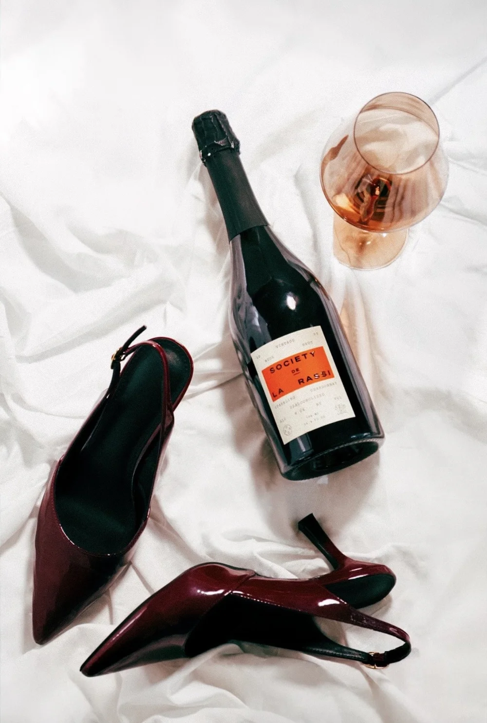 Editorial product photograph featuring sparkling wine and burgundy heels