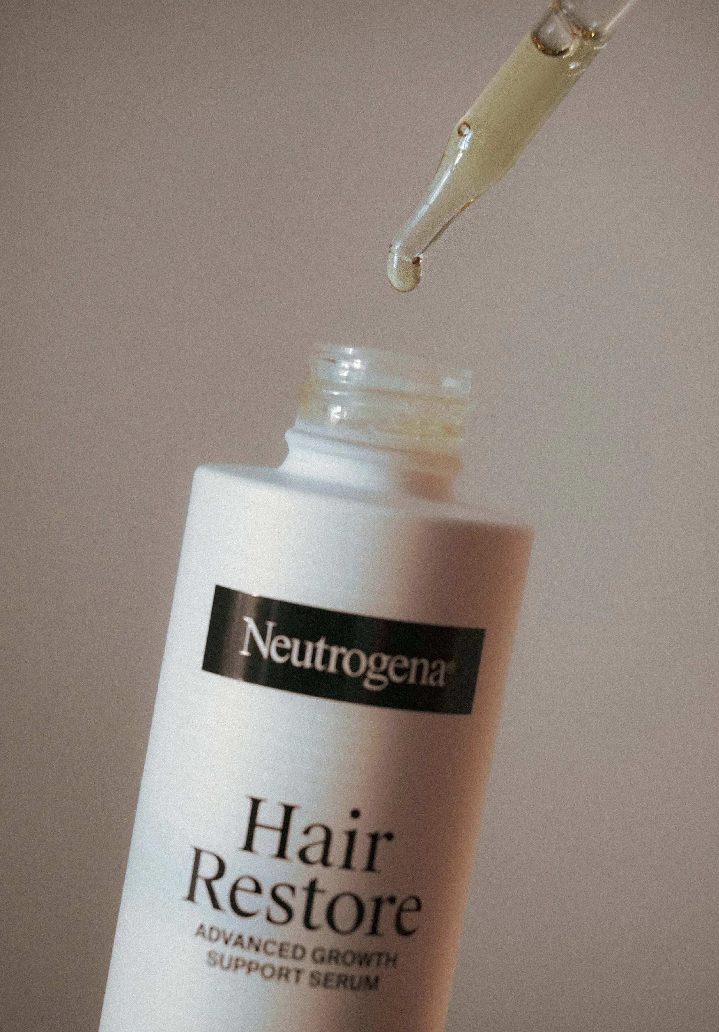 Close-up of a white bottle labeled 'Hair Restore' with a dropper releasing a drop of liquid into the bottle.