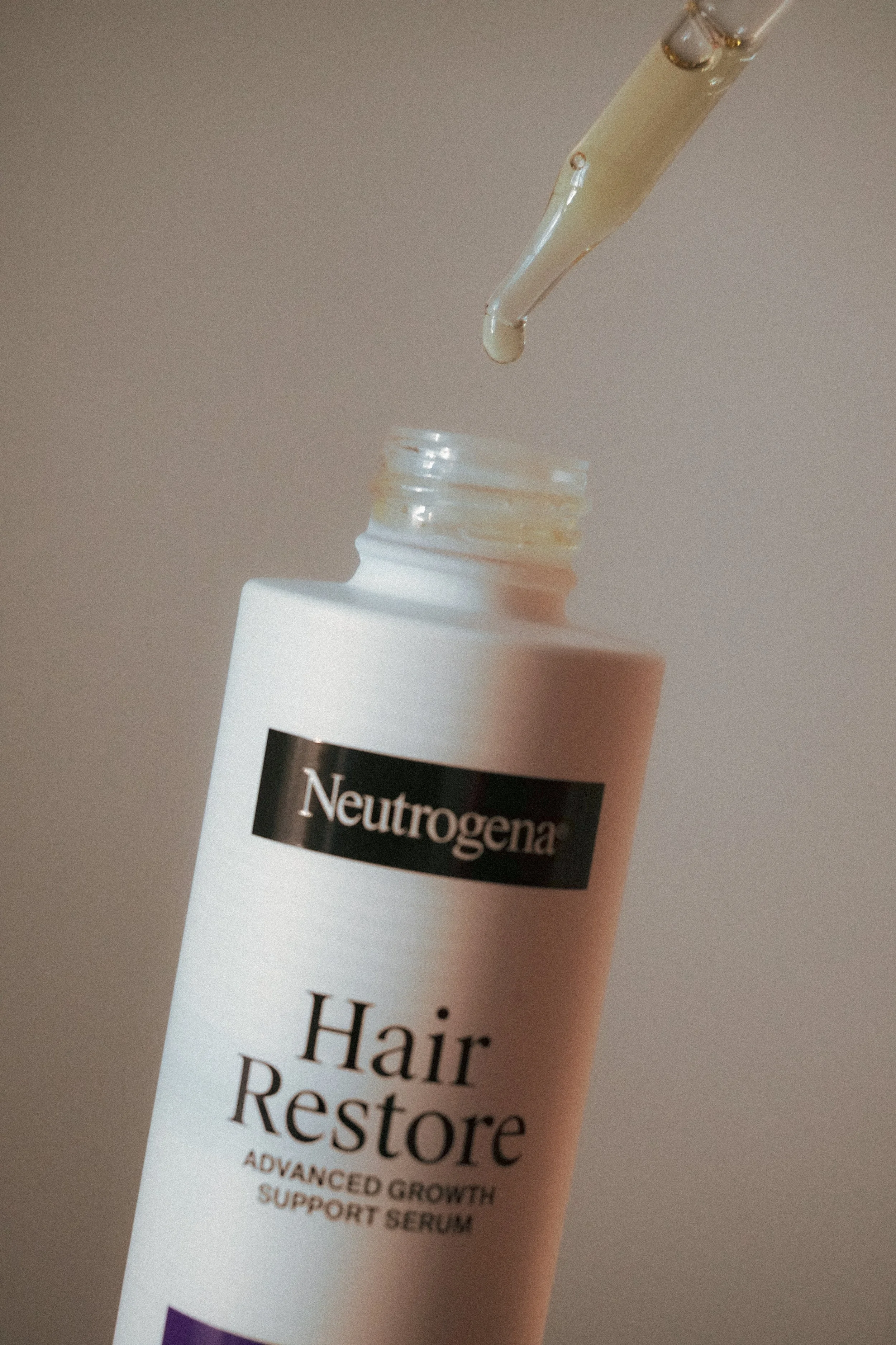 A white bottle of Neutrogena Hair Regrow Serum with an applicator dropping serum onto it.