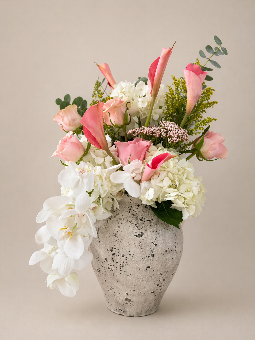 Elegan floral arrangement with blush calla lilies, hydrangeas, and orchids styled in a textured modern vessel.