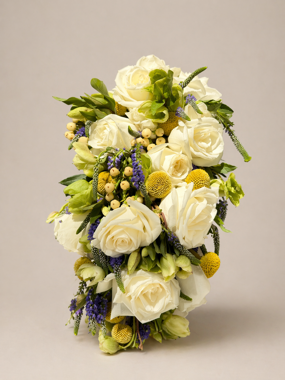 Modern floral arrangement featuring white roses, Veronica, billy buttons, and seasonal greenery in an elevated design.