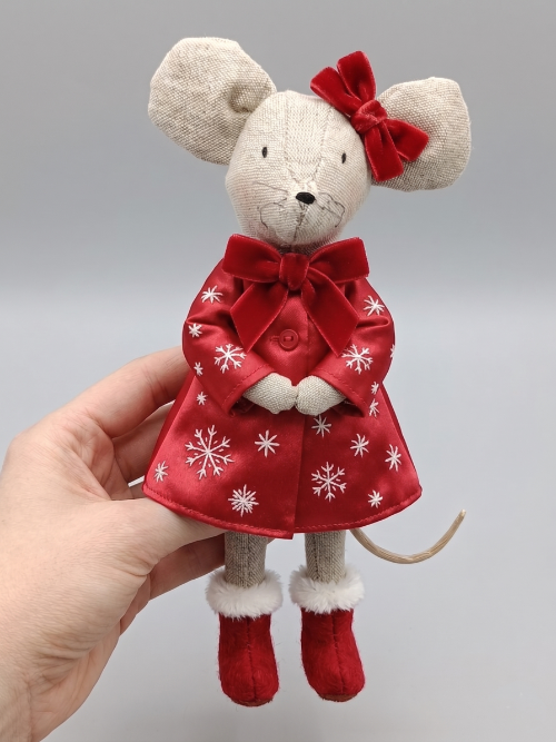 Hand holding a plush mouse doll dressed in a red Christmas dress with white snowflakes, red bow, and red boots, with a grey background.