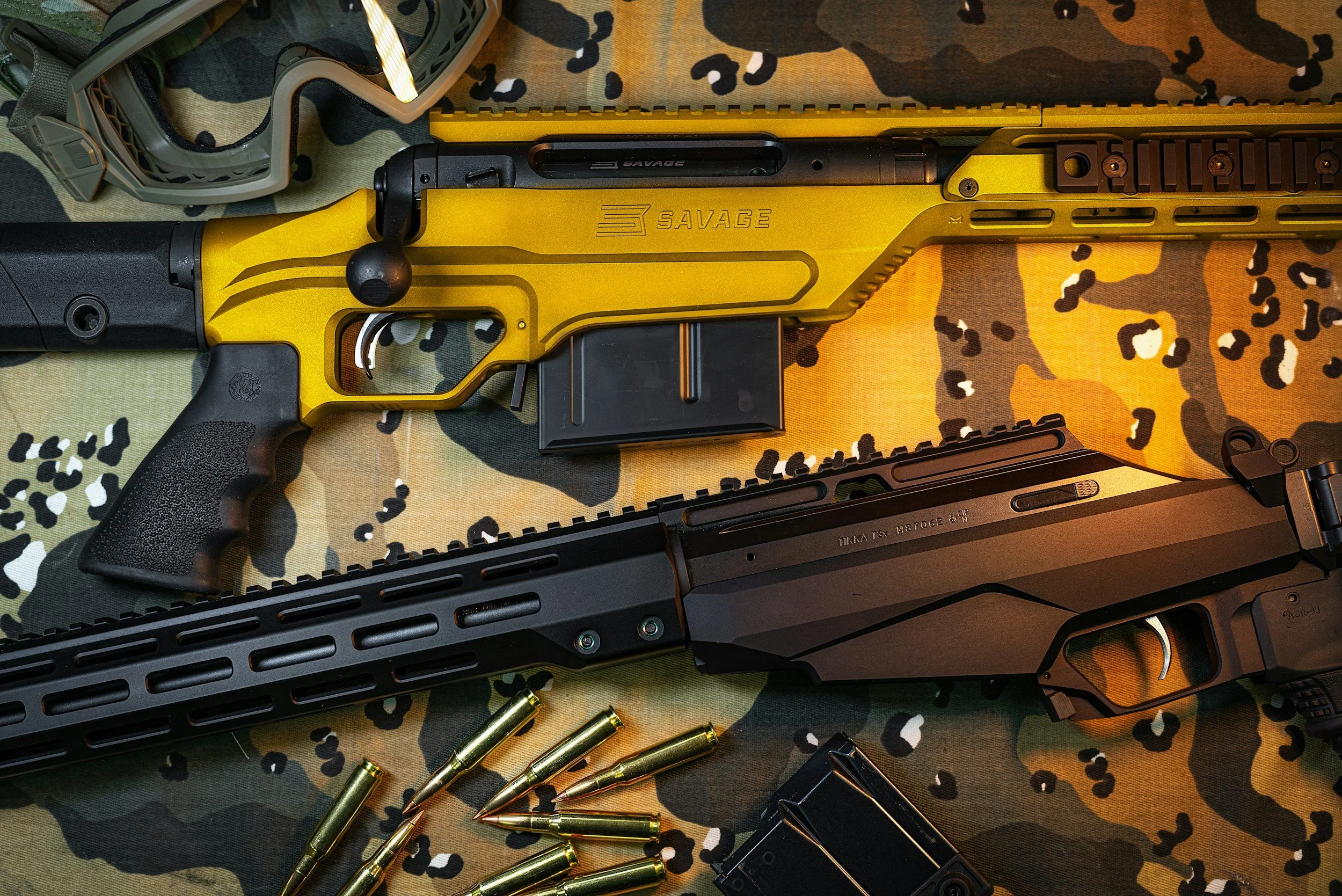 A yellow firearm with black accents on a camouflage-patterned fabric, surrounded by rifle magazines, bullets, and tactical glasses.