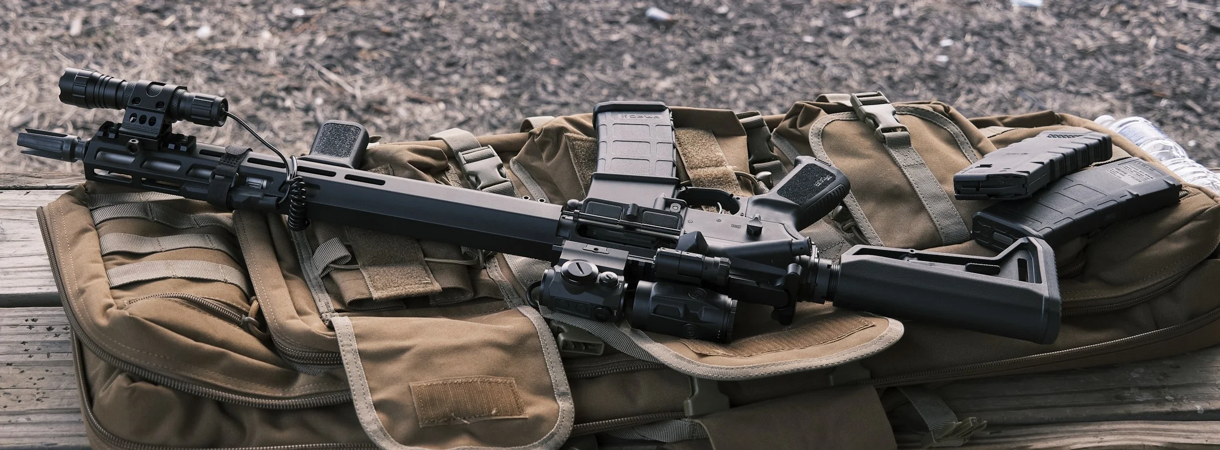 A firearm with a scope and accessories laid on a tactical bag on a wooden surface.