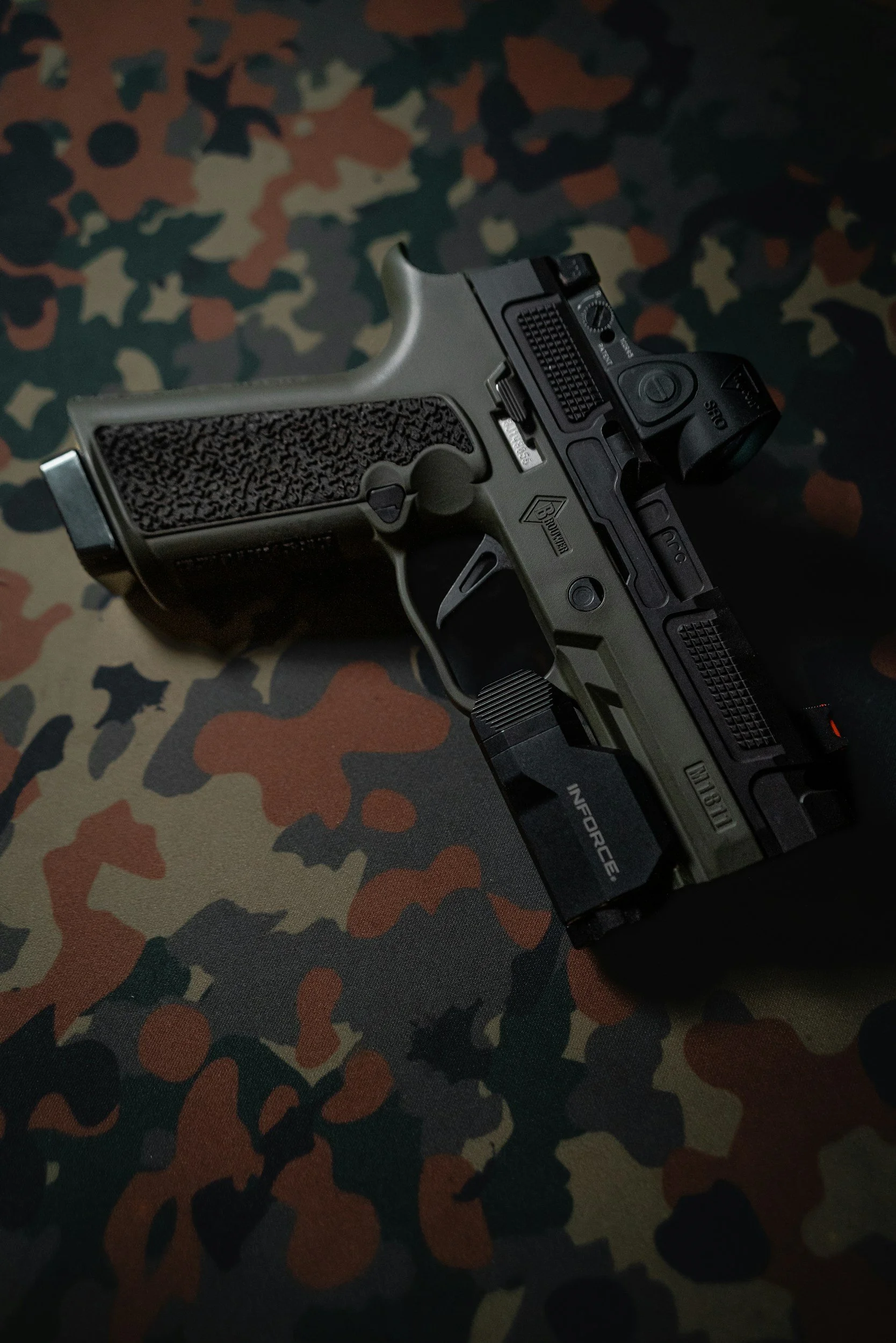 A handgun with a green and black design resting on a camouflage-patterned fabric.