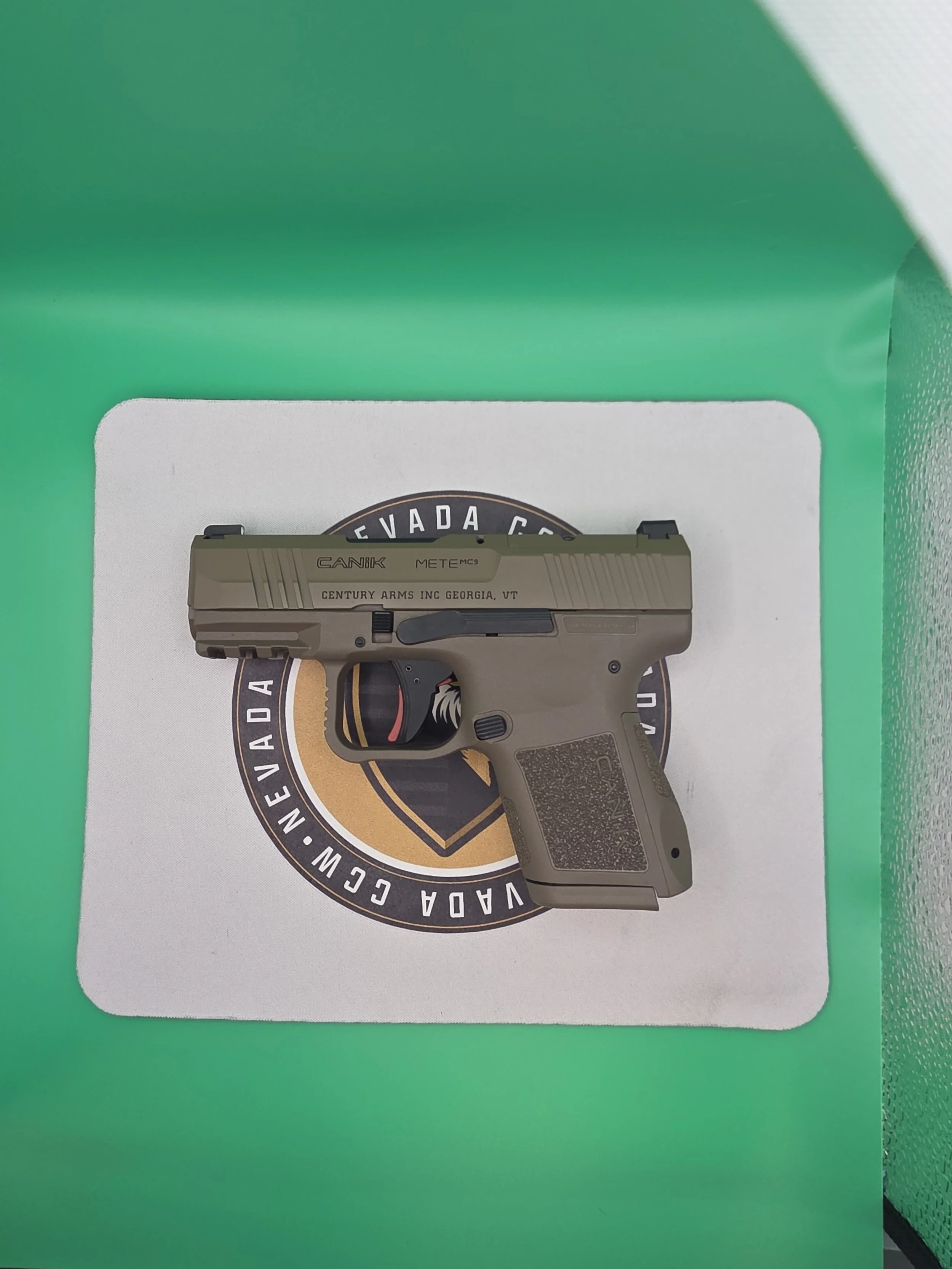 Close-up of a gun partially obscured by a green wall, with a round badge that reads 'Nevada County, California' underneath.