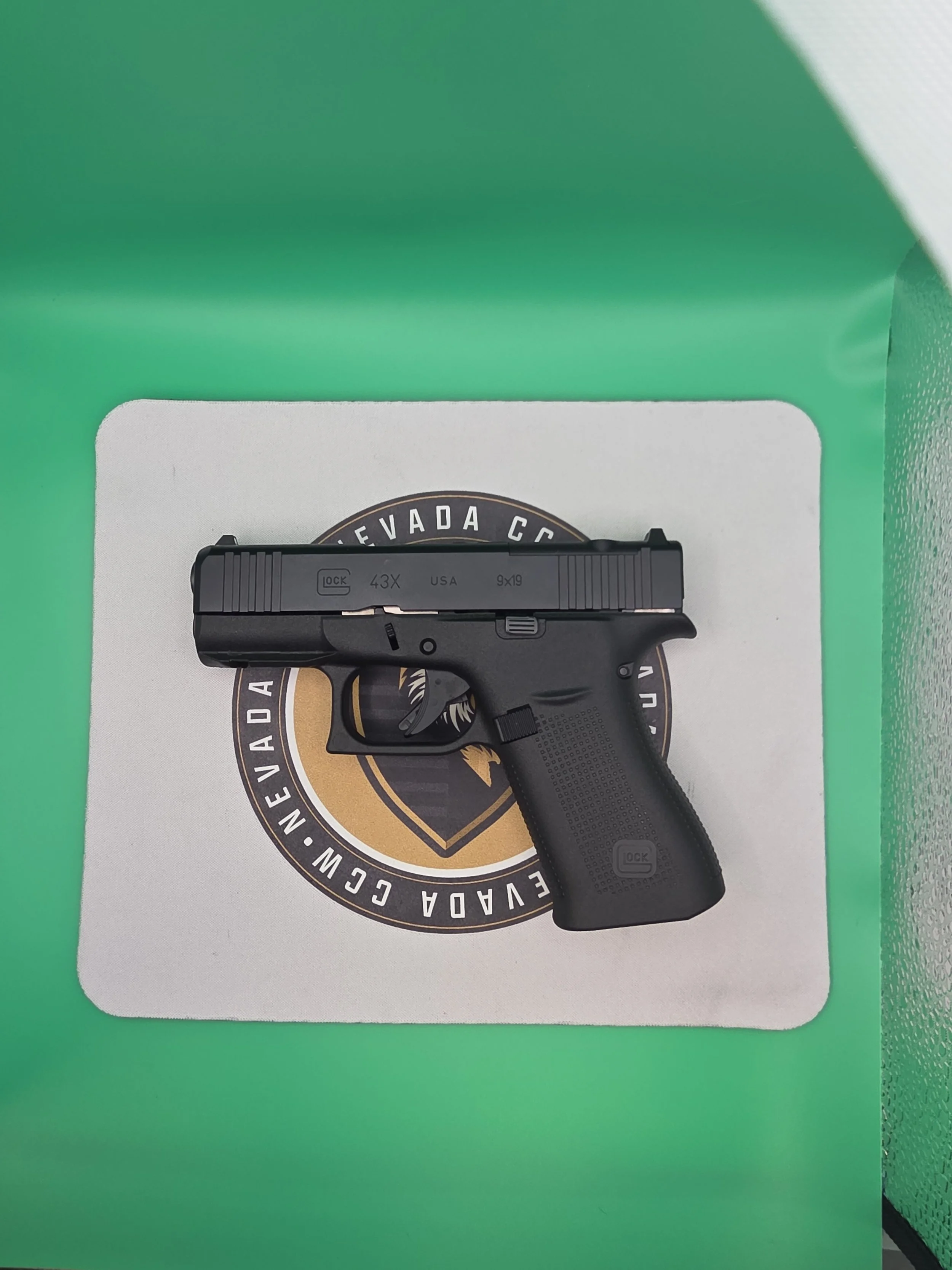 A black Glock handgun resting on a white surface with a round emblem that reads "Evada CC" in black and gold.