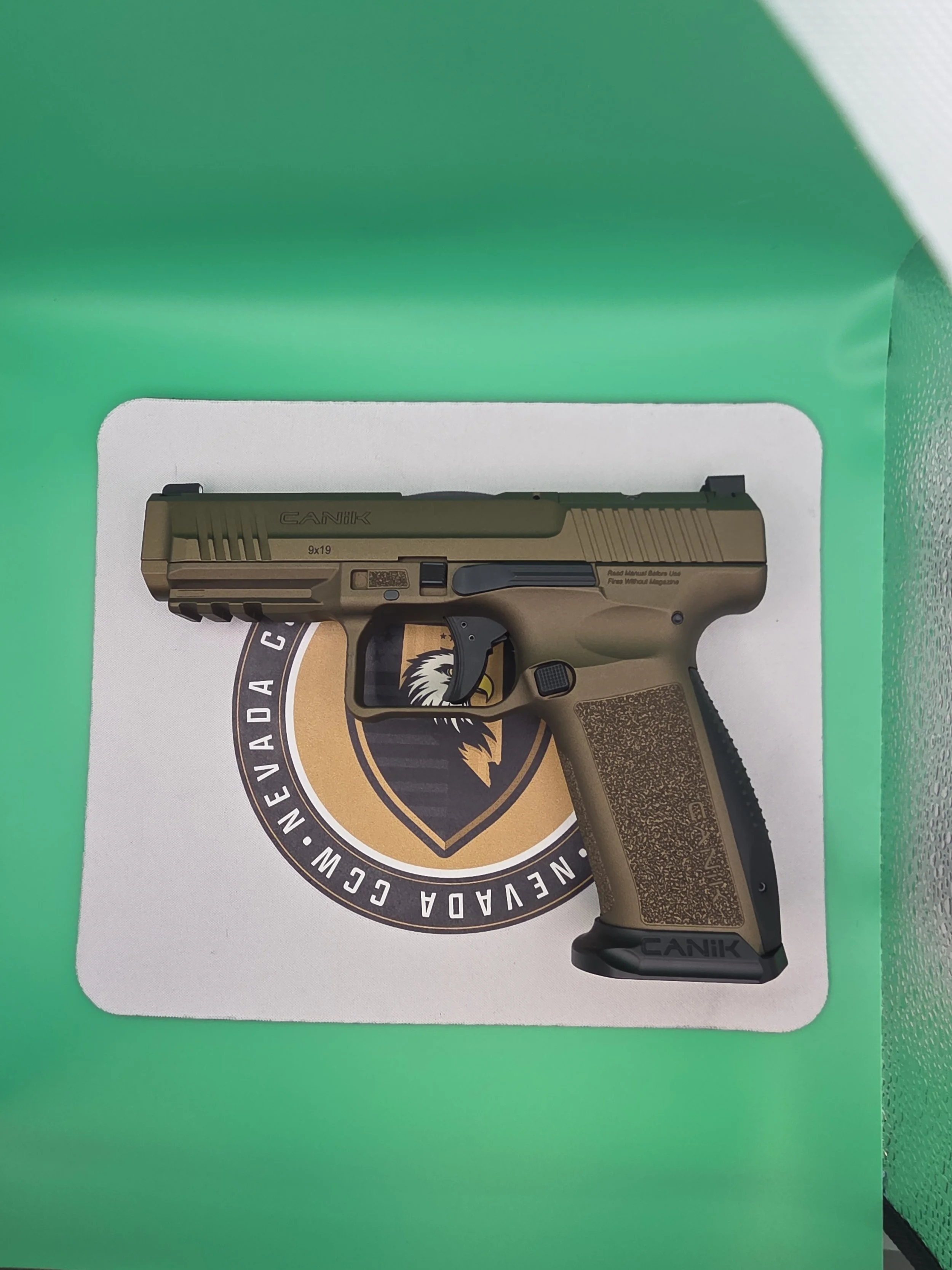 Box featuring a tan and black CANIK Glock style pistol with a textured grip, sitting on a card with a circular emblem of an eagle and the words Nevada Guard.
