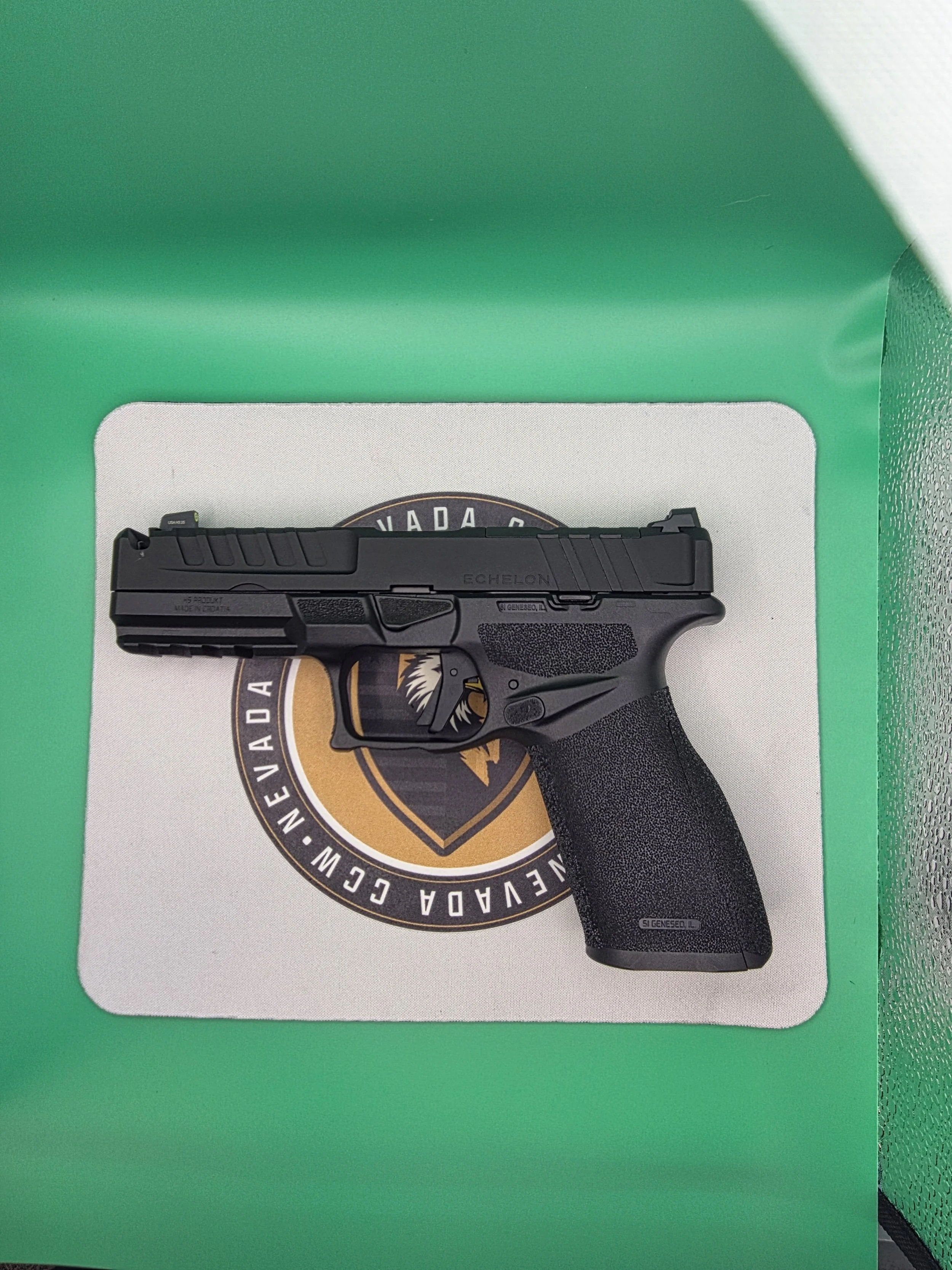 Close-up of a black handgun placed on a white surface with a logo, inside a green box or case.